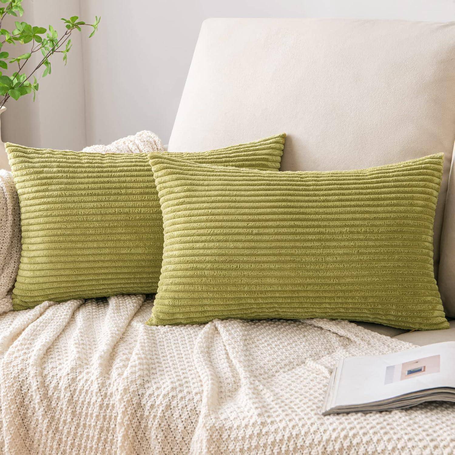 Ein gemütliches Wohnzimmer mit einem beigen Sofa, das mit einer strukturierten Decke überzogen ist. Zwei grüne strukturierte Kissen lehnen an der Rückenlehne. Eine kleine Pflanze und eine Zeitschrift in der Nähe verleihen dem Raum eine dekorative Note.