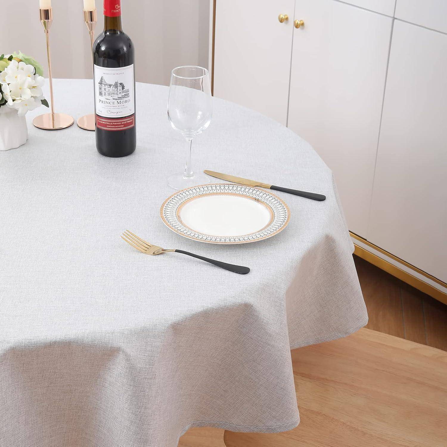 Ein runder Tisch für eine Person, gedeckt mit einer grauen Tischdecke, einer Weinflasche, einem leeren Weinglas und einem weißen Teller mit Gabel und Messer.
