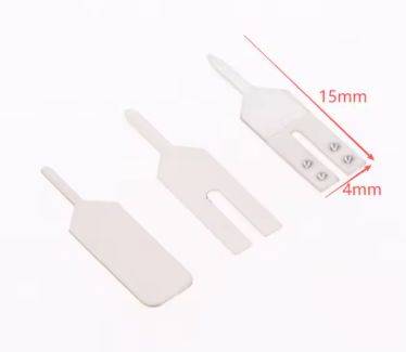 Drei weiße Plastikwerkzeuge mit unterschiedlichen Formen und Größen, eines davon mit Maßangaben von 15 mm x 4 mm.