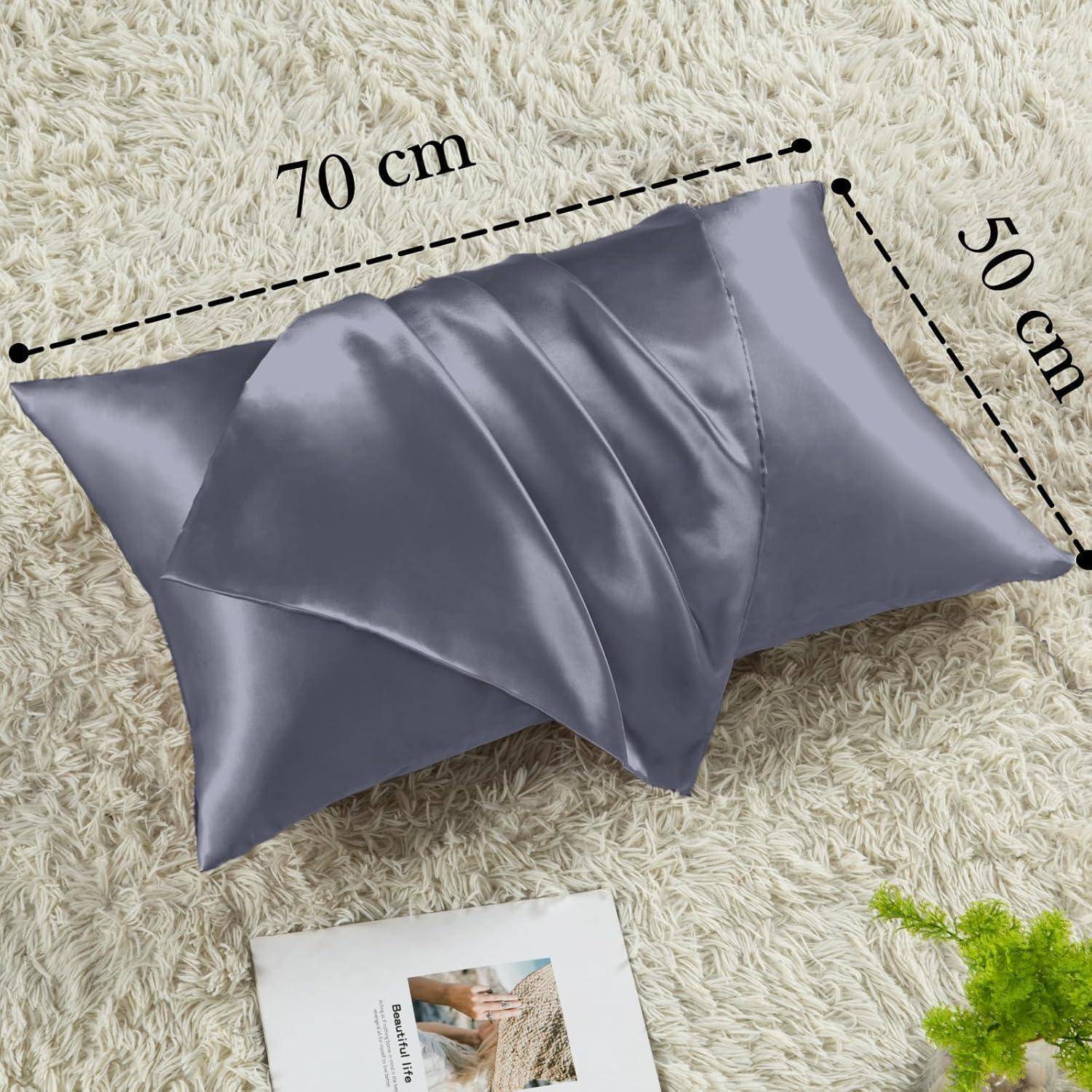Ein grauer Kissenbezug mit Satin-Überzug, der 70 cm x 50 cm misst, liegt auf einem beigen Teppich neben einer aufgeschlagenen Zeitschrift mit Einrichtungsthemen.