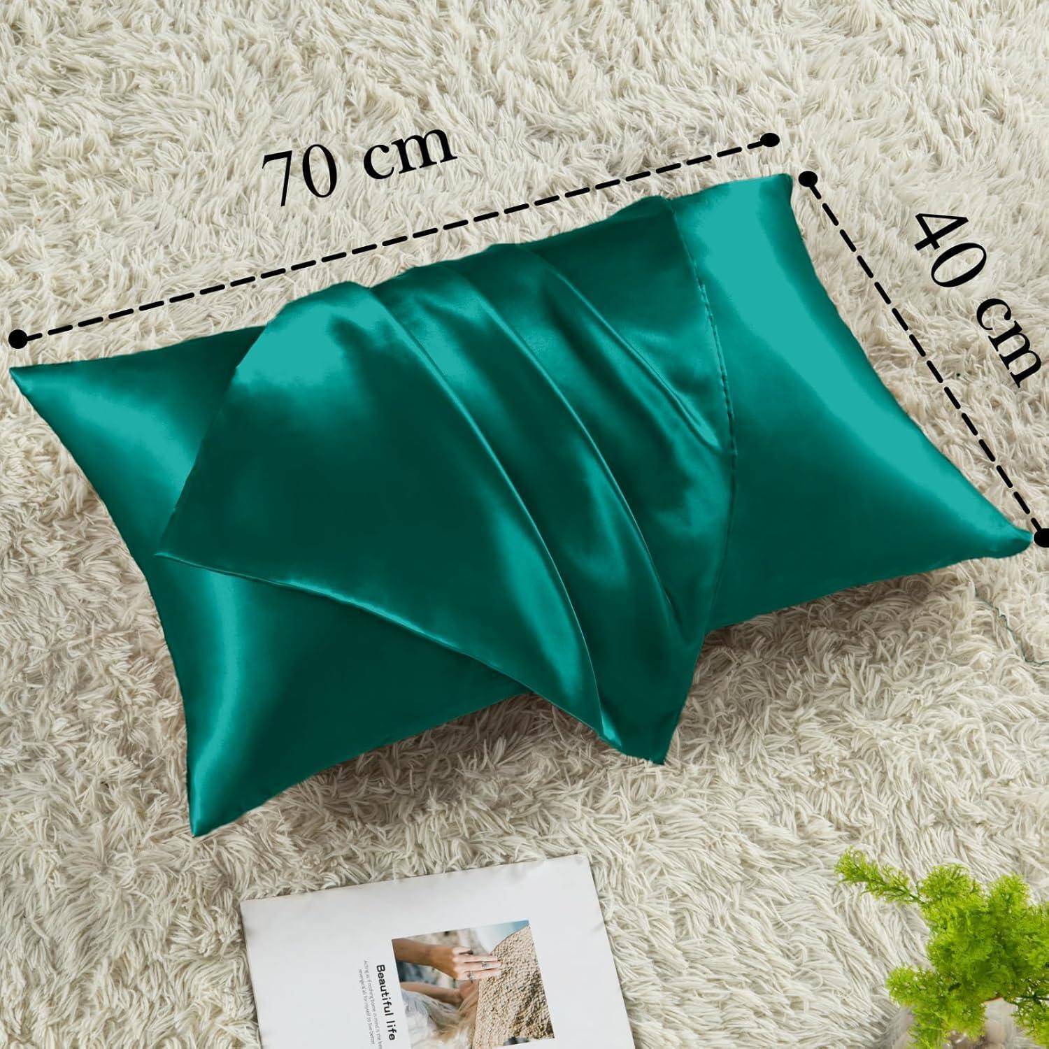 Eine türkisfarbene Seidenkissenhülle mit den Maßen 70 cm x 40 cm liegt auf einer hellfarbigen, strukturierten Oberfläche. Ein Faltblatt ist teilweise darunter sichtbar.