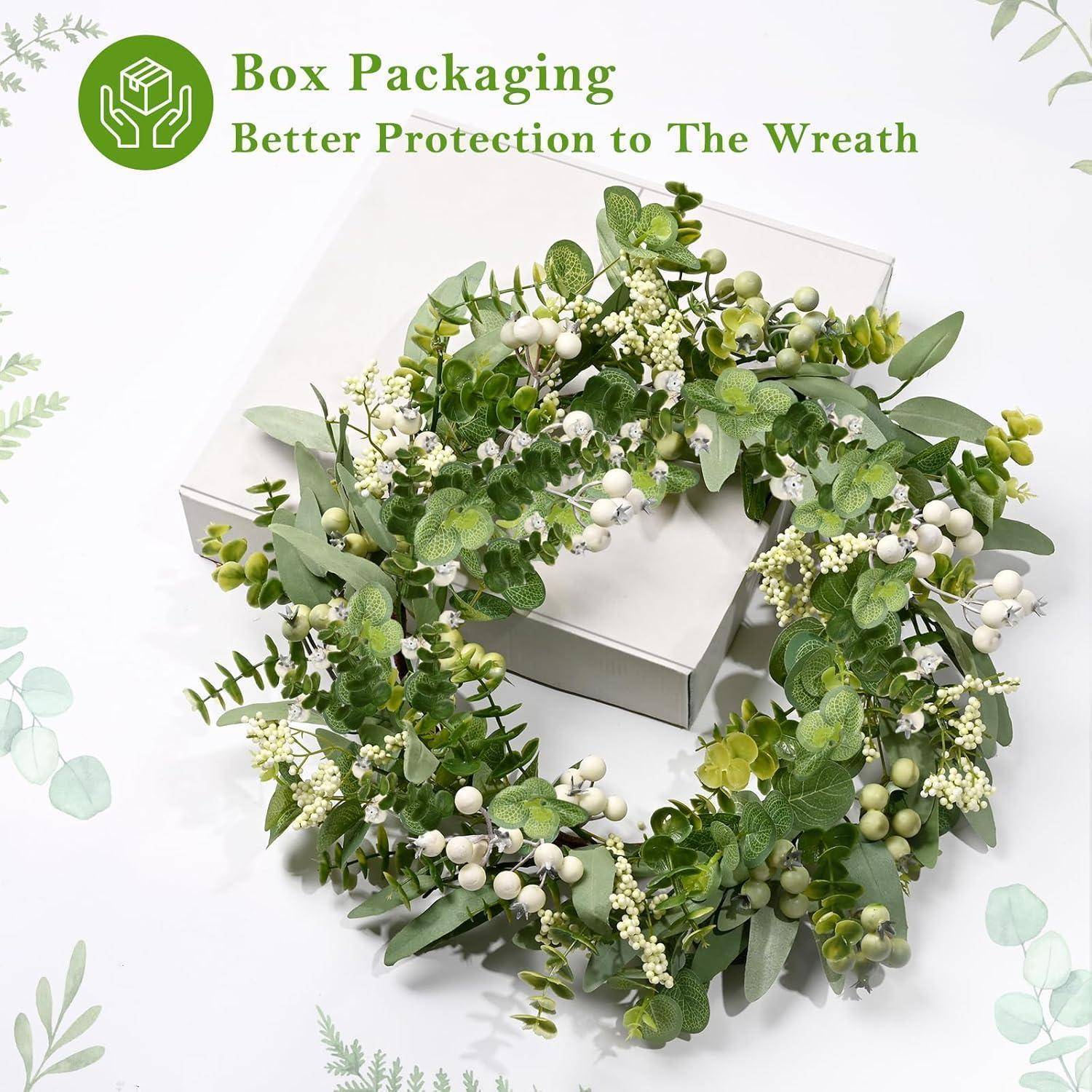 Ein zarter grün-weißer Kranz, geschmückt mit kleinen weißen Beeren und Blättern, ist auf einer weißen Verpackungsbox platziert. Der Text lautet: 