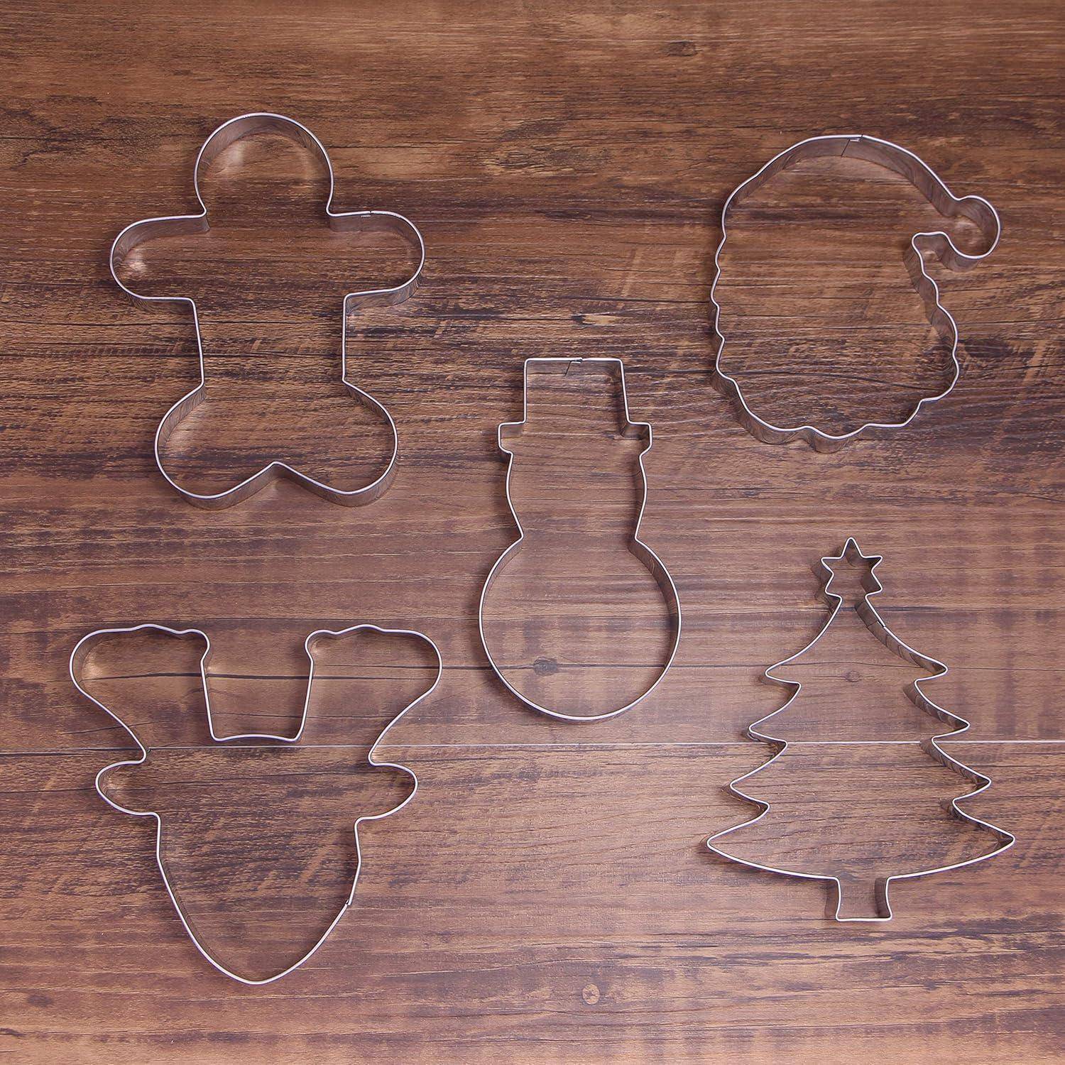 Fünf Metall-Ausstechformen auf Holz: Lebkuchenmann, Weihnachtsmann-Gesicht, Schneemann, Rentierhaupf und Weihnachtsbaum-Formen.