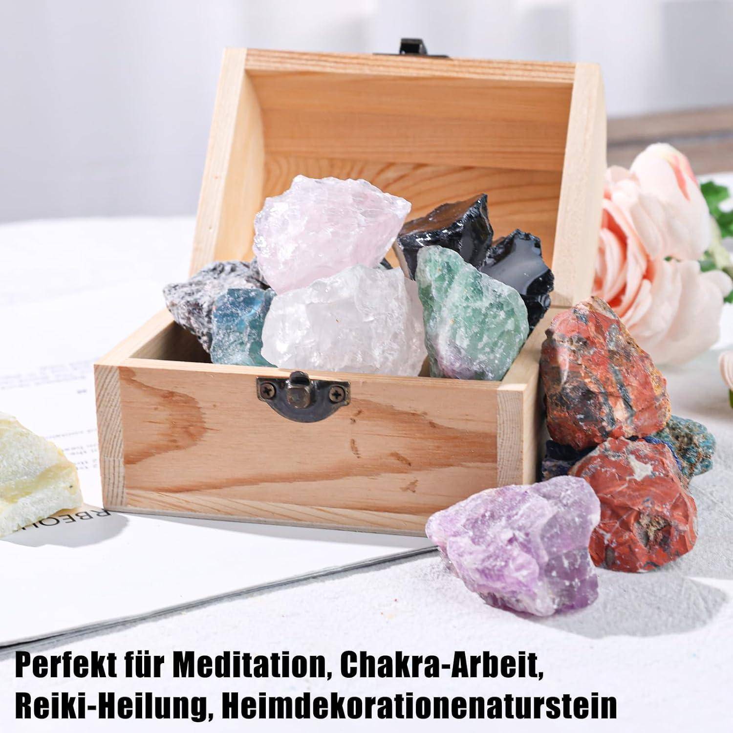 Eine offene Holzkiste gefüllt mit bunten Kristallen auf einem Tisch mit Text auf Deutsch über Meditation und Heimdekoration.