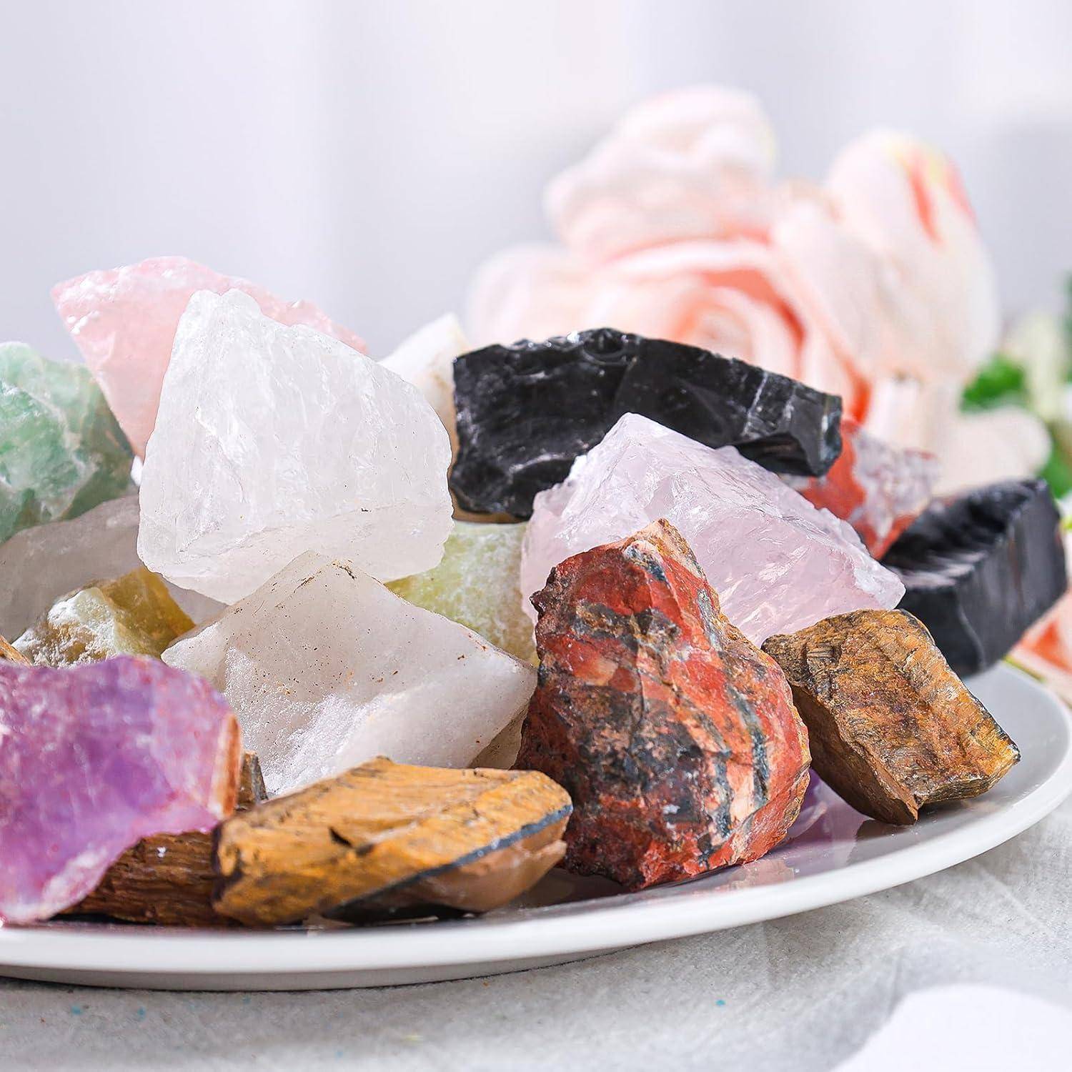 Eine Platte mit verschiedenen farbenfrohen Mineralsteinen, darunter rosa, schwarz und orange, vor einem Hintergrund aus weichen rosa Blüten.
