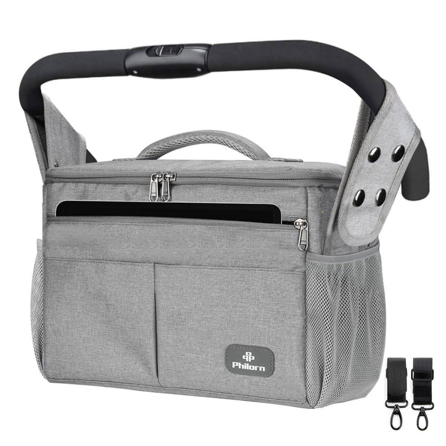 Eine graue Kinderwagen-Organizer-Tasche, die an den Griffen befestigt ist, mit Fächern und Taschen. Inklusive eines Getränkehalters und zwei zusätzlicher Riemen.