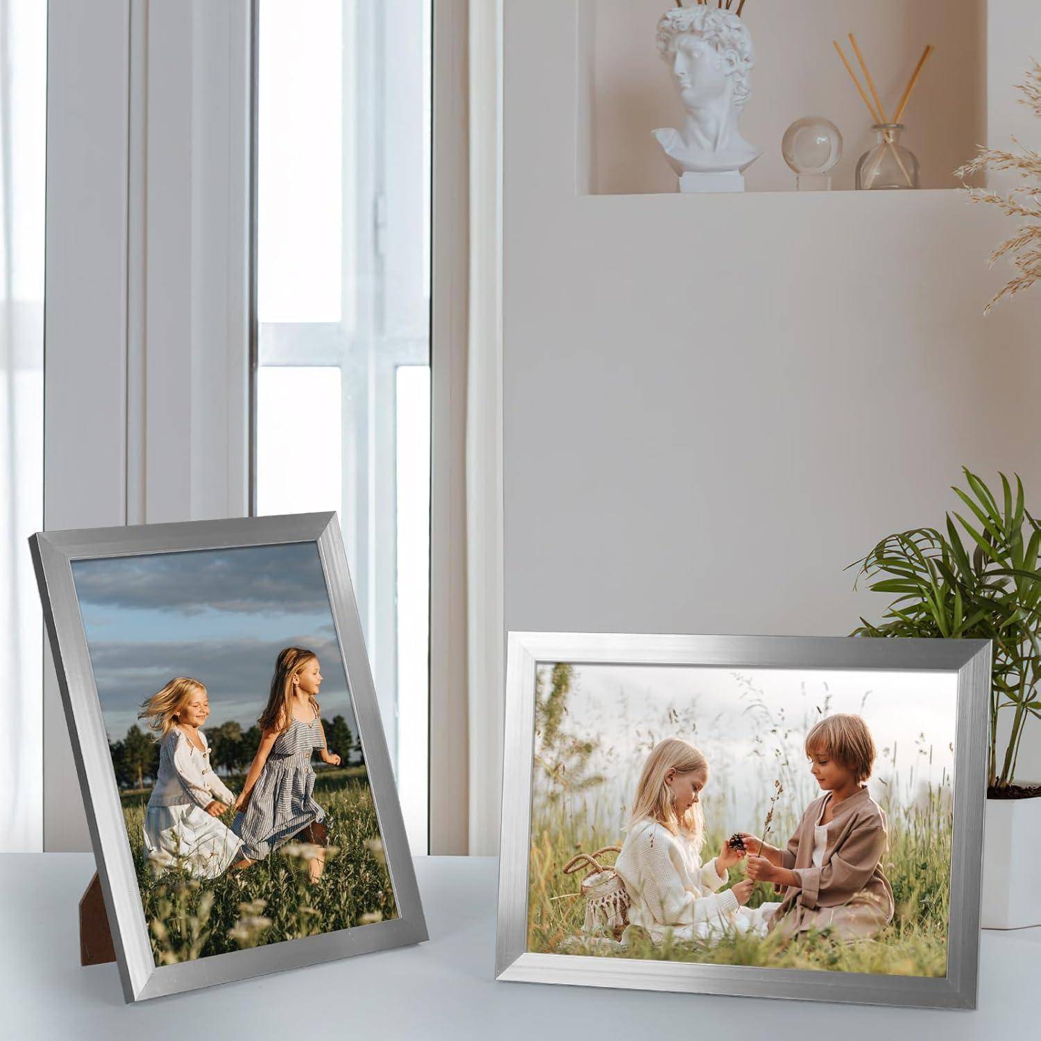 Gerahmte Fotos auf einem Tisch: Das linke Foto zeigt zwei Mädchen in Kleidern, die durch ein Feld laufen; das rechte Foto stellt zwei Kinder dar, die auf dem Gras sitzen.
