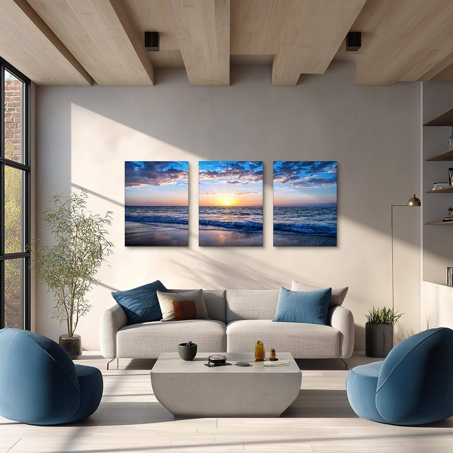 Wohnzimmer mit moderner Einrichtung, das eine Couch, blaue Sessel und ein Triptychon eines Sonnenuntergangs über dem Ozean umfasst und eine ruhige Atmosphäre erzeugt.
