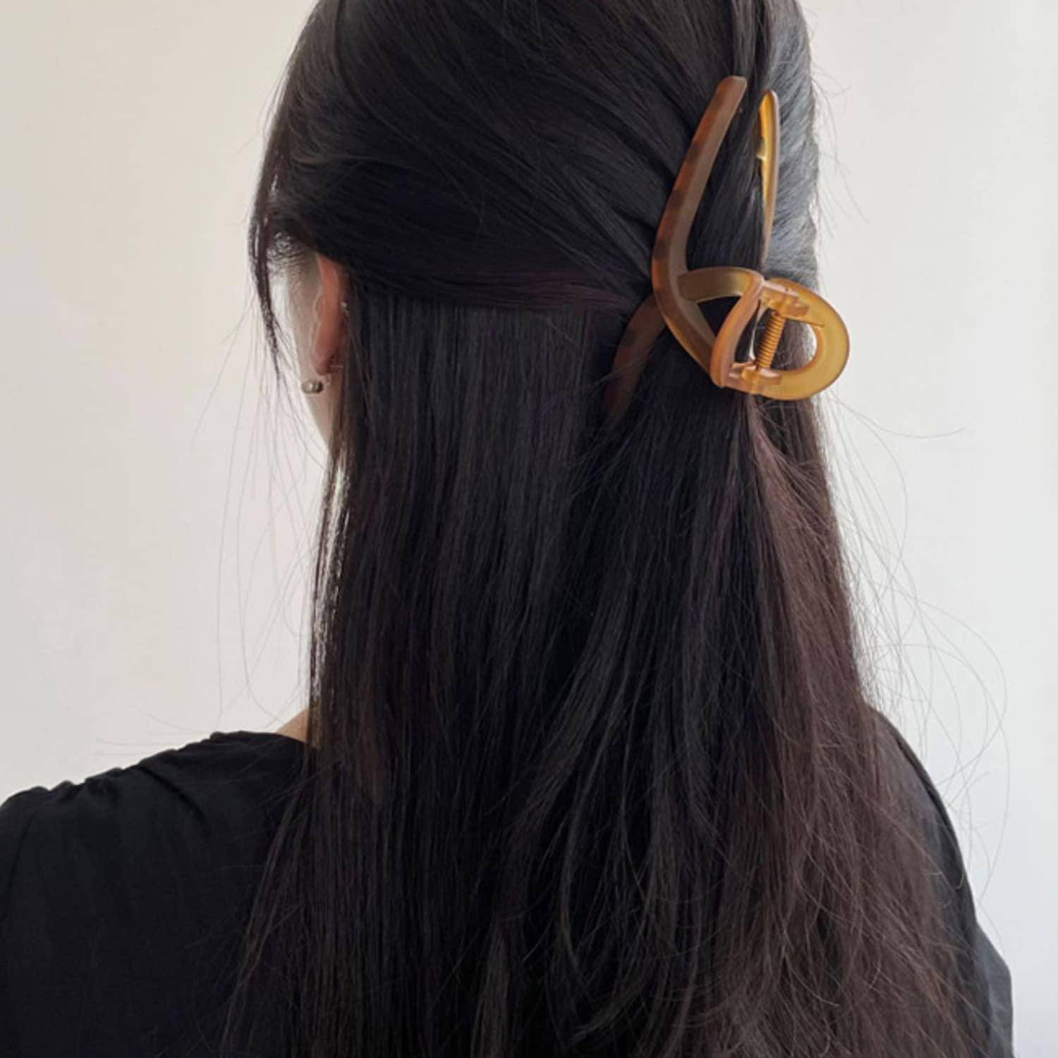 Eine Person mit langen dunklen Haaren, die in einer Hochsteckfrisur getragen werden, halb hochgesteckt und halb offen, und mit einer großen braunen Haarspange am Hinterkopf befestigt.