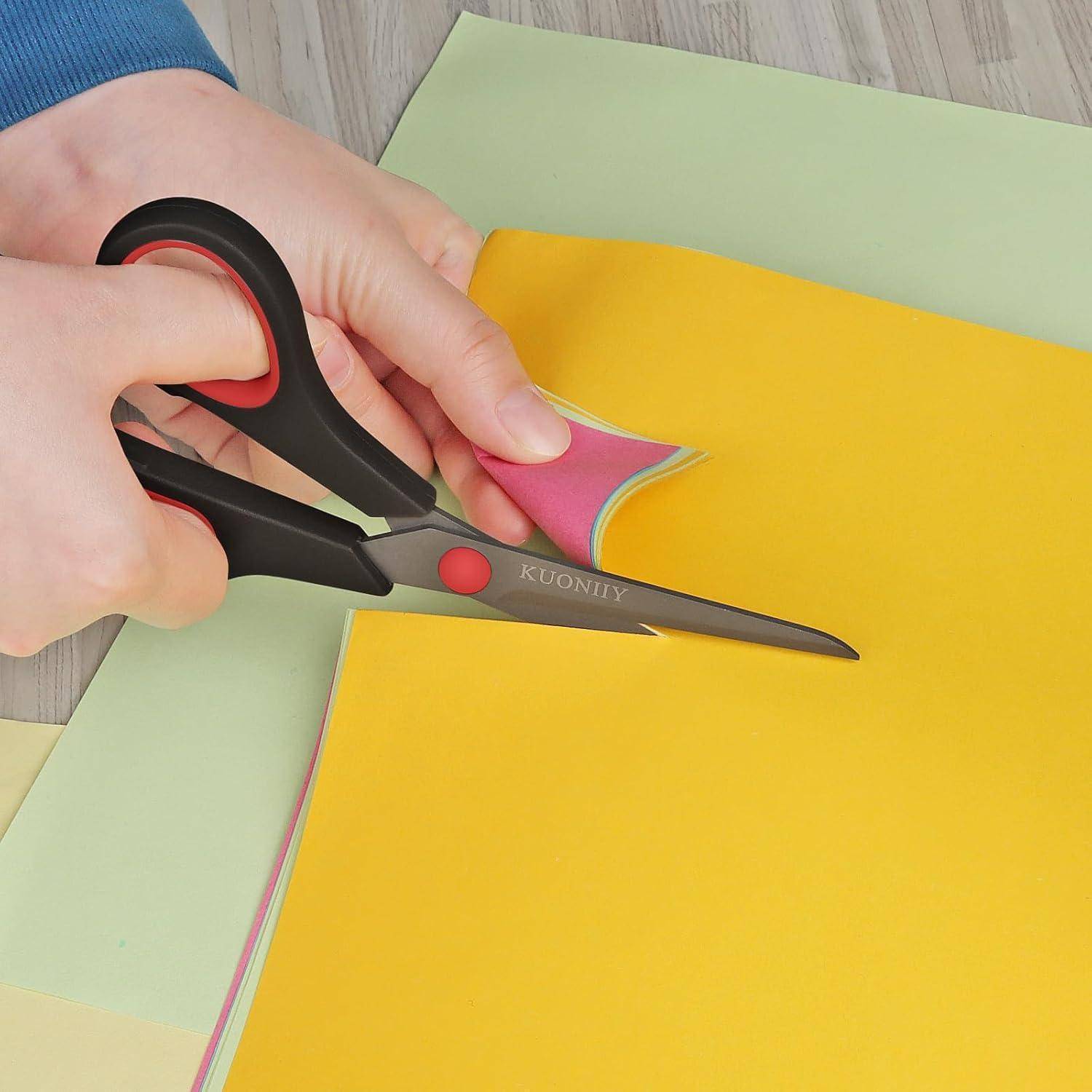 Hände, die buntes Papier mit schwarzer und roter Schere auf einem Holztisch schneiden.