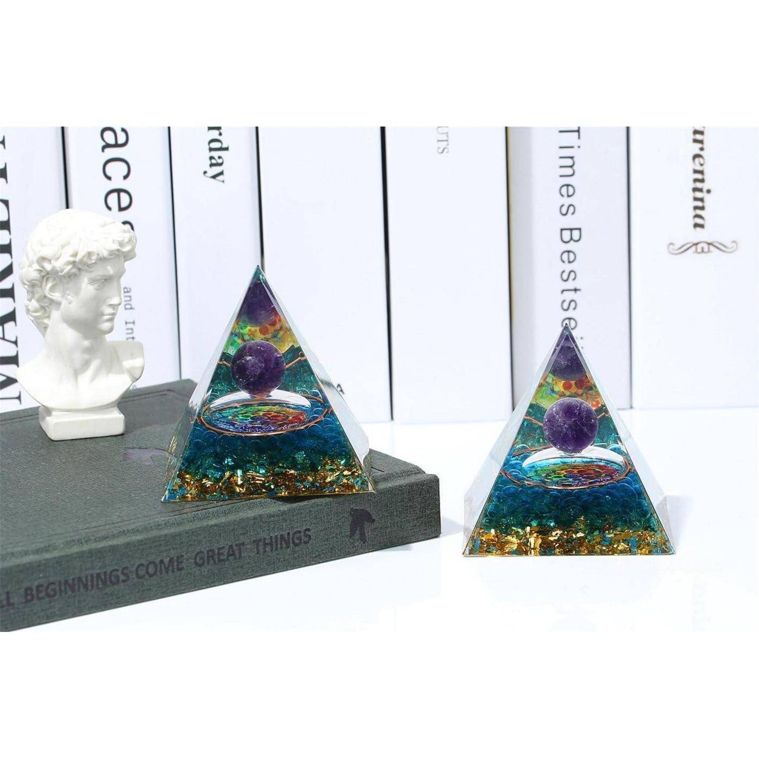 Zwei pyramidenförmige Orgonit-Skulpturen mit bunten Schichten und einer Kugel im Inneren, auf einem Buch mit dem Titel 