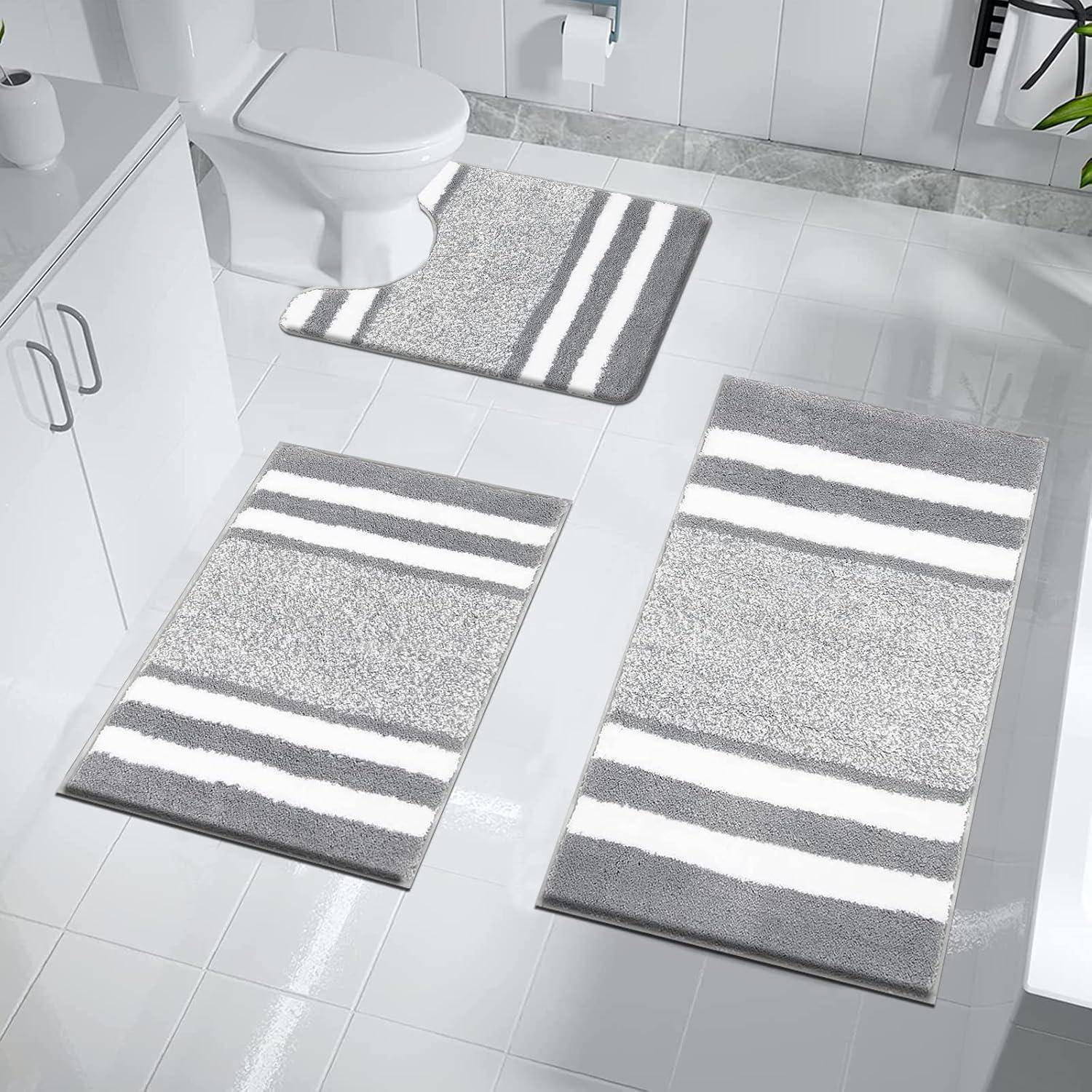 Badezimmerset mit drei grauen und weißen gestreiften Teppichen, die in der Nähe von Toilette und Waschbecken platziert sind, vor einem weißen gefliesten Boden und einer weißen Wand.
