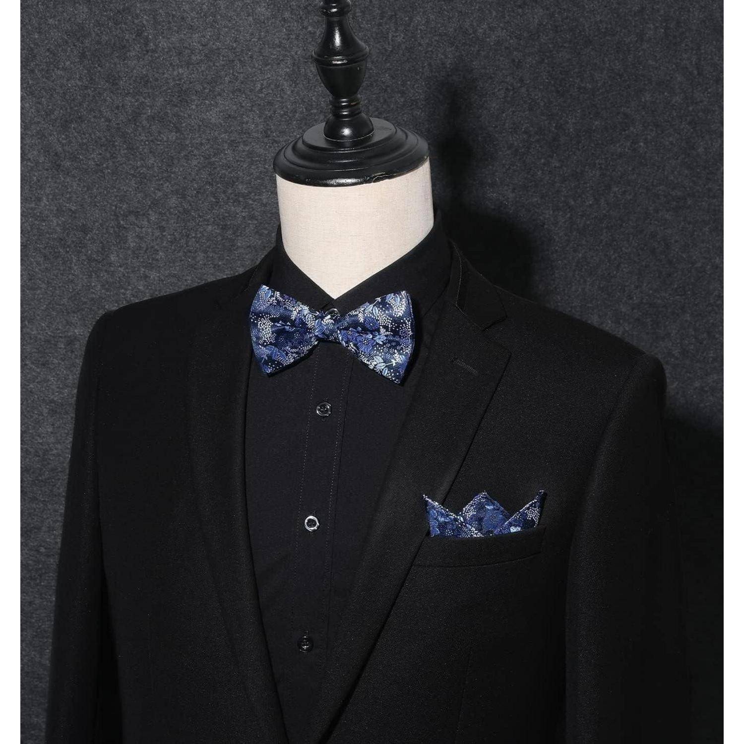 Mannequin, der einen schwarzen Anzug mit einer blauen Blumenfliege und dem passenden Einstecktuch trägt, vor einem dunklen Hintergrund präsentiert.