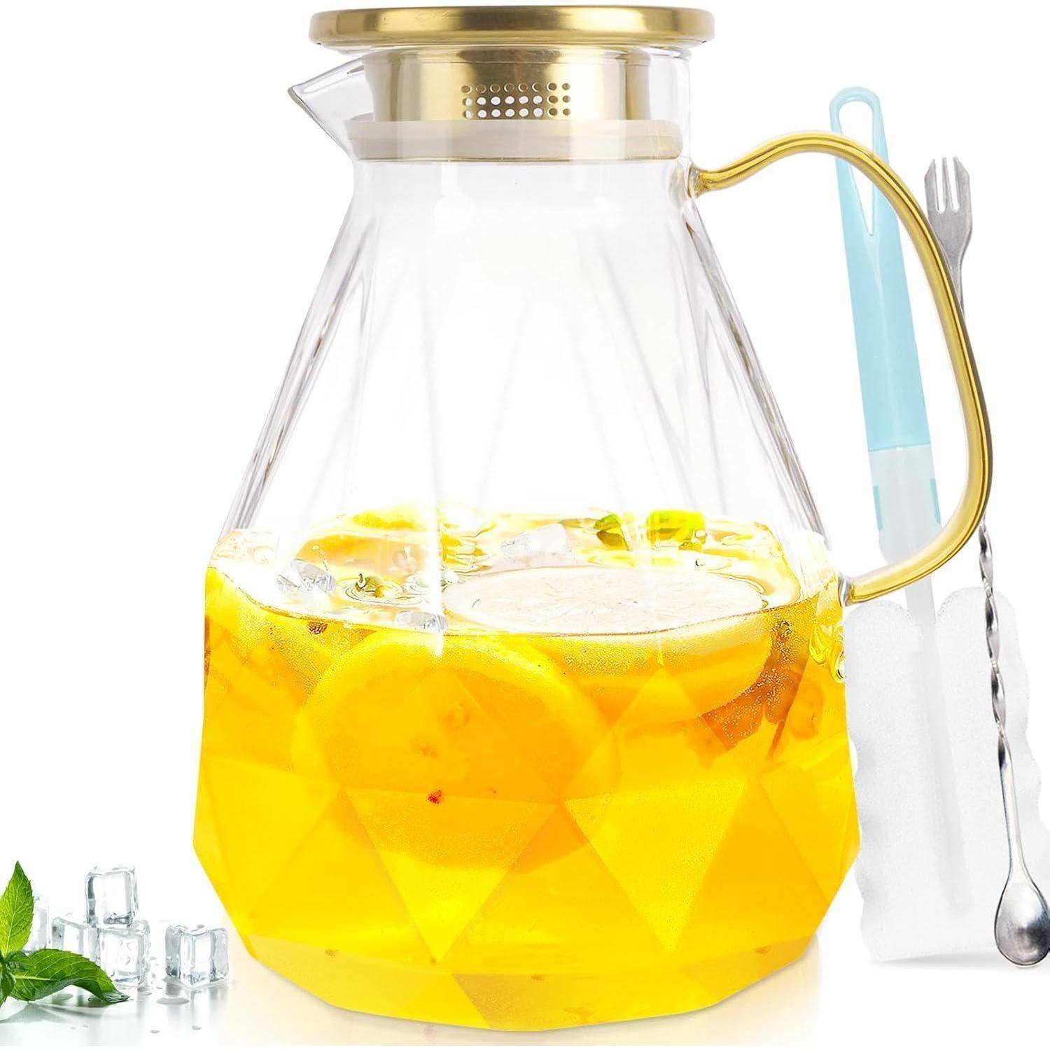 Ein Glaskrug mit einem goldenen Deckel enthält gelbe Limonade mit Zitronenscheiben. Eiswürfel befinden sich in der Nähe, zusammen mit einem Minzzweig und Utensilien.
