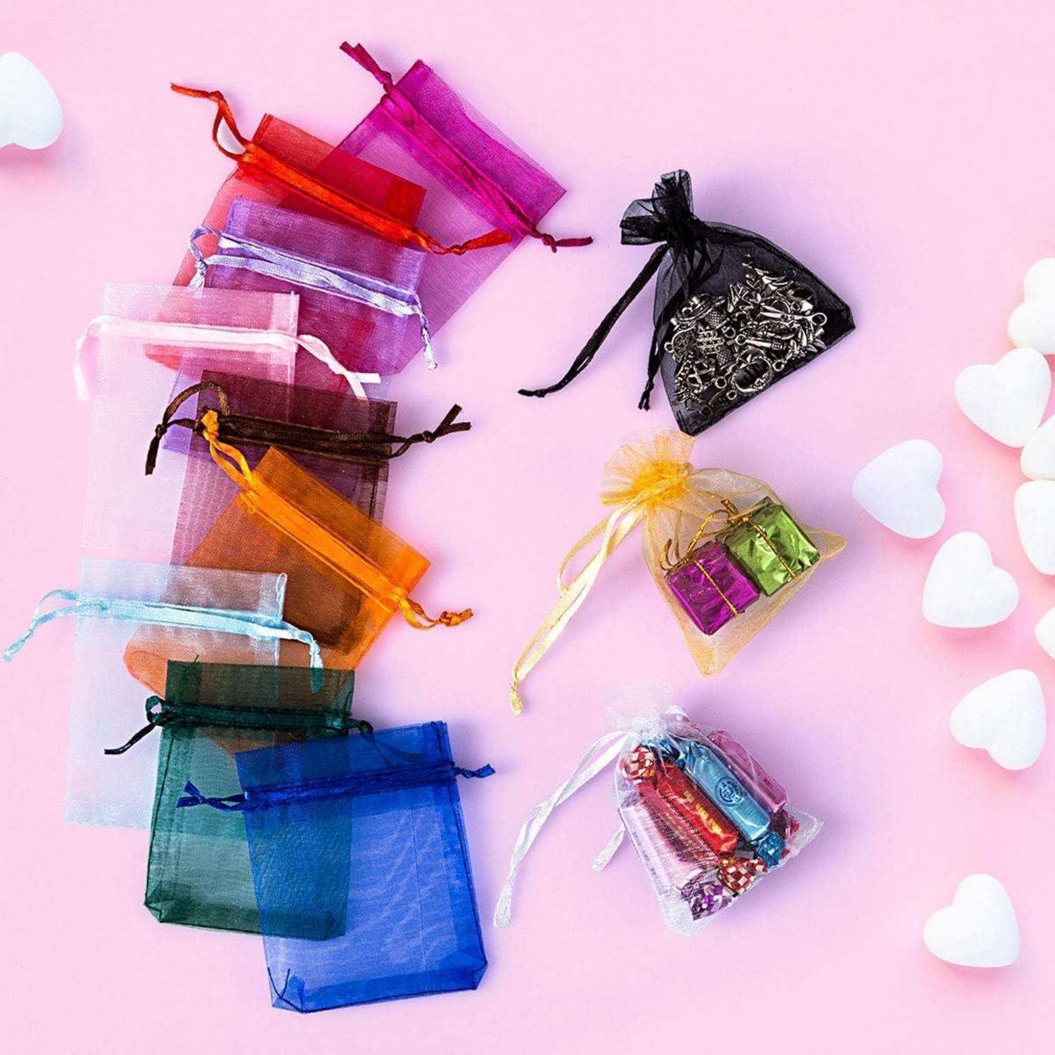 Bunte Geschenkbeutel mit Kordelzug sind auf einer rosa Oberfläche angeordnet, einige davon gefüllt mit Schmuck und Kleinigkeiten. Weiße Herzdekorationen sind in der Nähe verstreut.