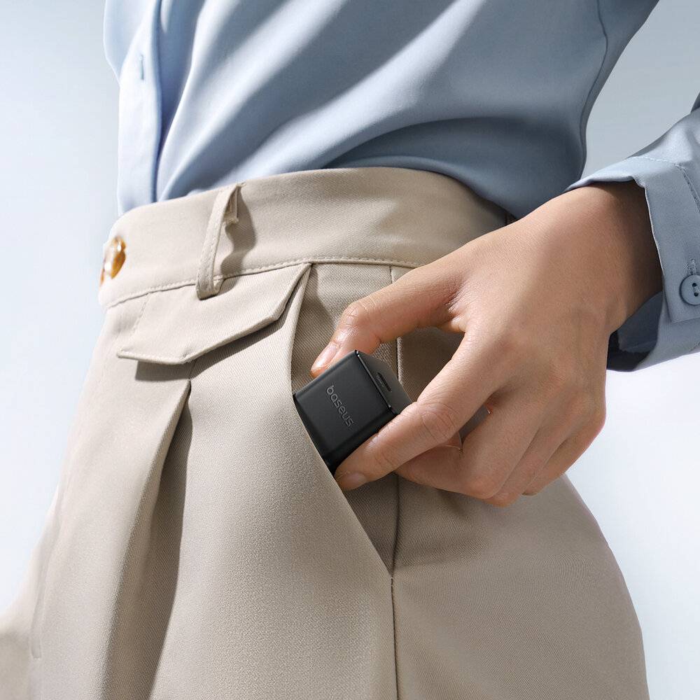 Eine Person in einem hellblauen Hemd und beigefarbener Hose steckt ein kleines schwarzes elektronisches Gerät in ihre Tasche und zeigt damit seine tragbare Größe.