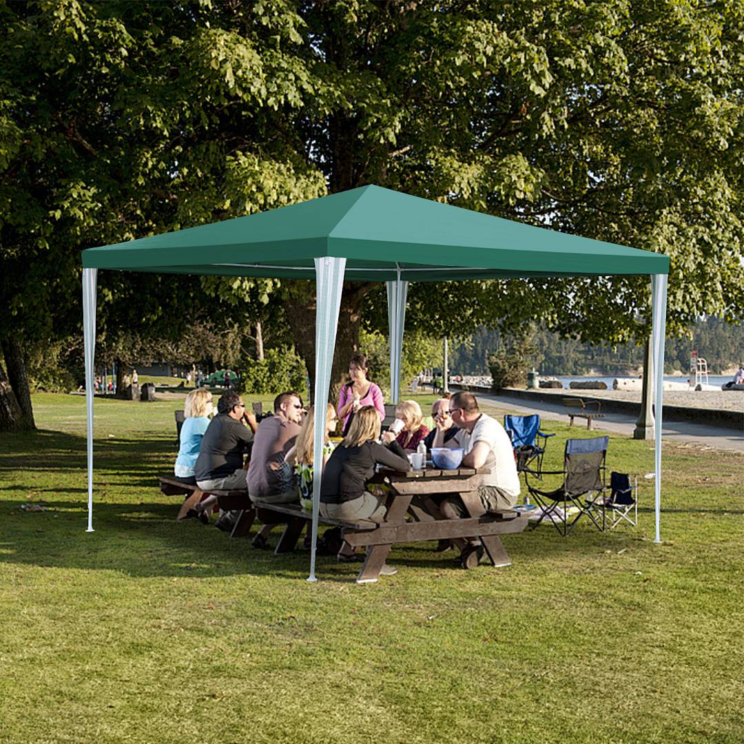 Eine Gruppe von Menschen sitzt an Picknicktischen unter einem grünen Baldachin in einem Park, plaudert und genießt einen sonnigen Tag in der Nähe eines Sees.