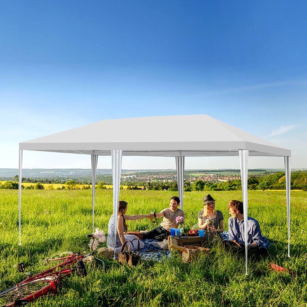 Vier Menschen genießen ein Picknick unter einem großen weißen Sonnensegel in einem grasbedeckten Feld, mit Fahrrädern in der Nähe und einer malerischen Aussicht im Hintergrund.