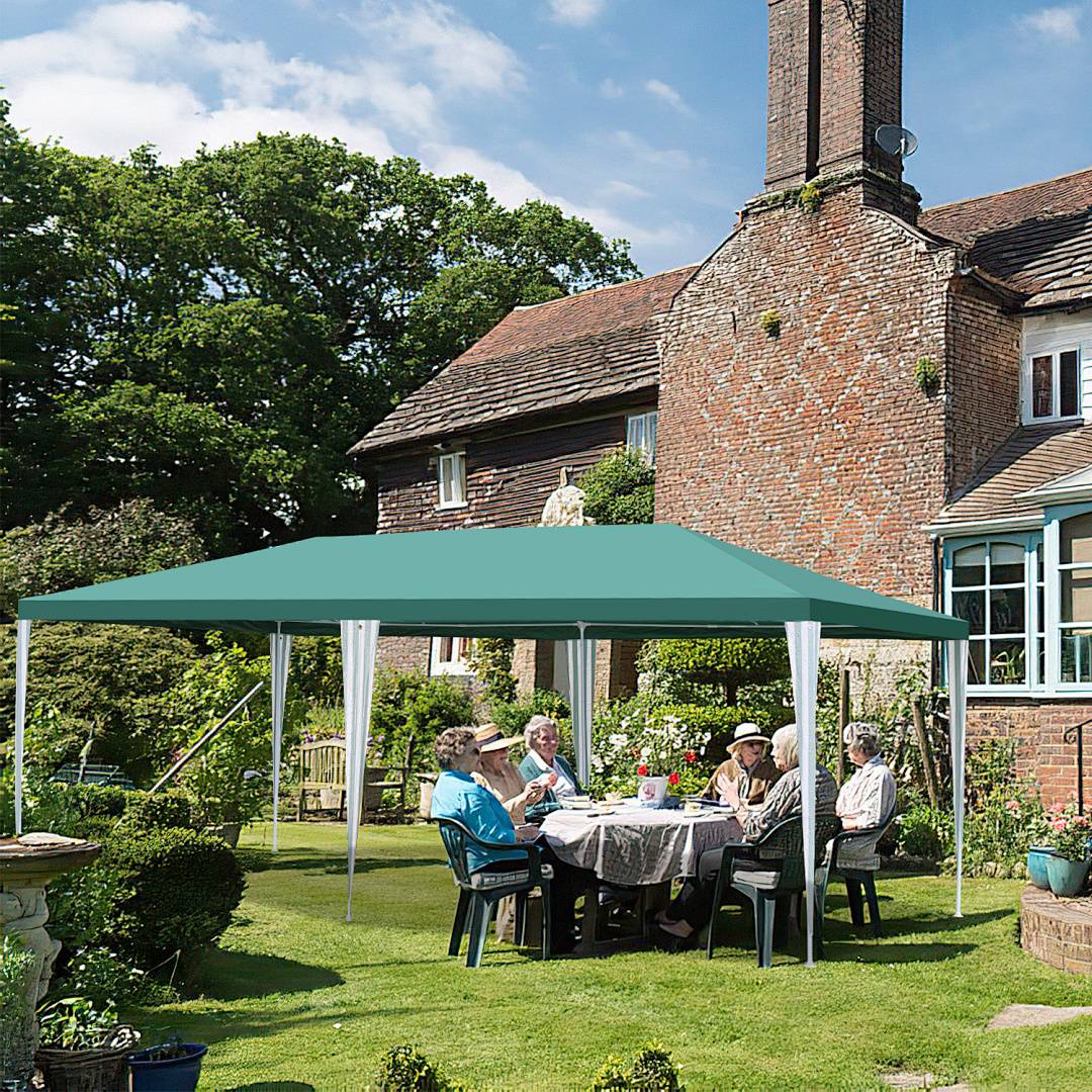 Eine Gruppe von Menschen, die um einen Tisch unter einem Pavillon in einem Garten sitzen, neben einem Backsteinhaus mit Bäumen im Hintergrund.