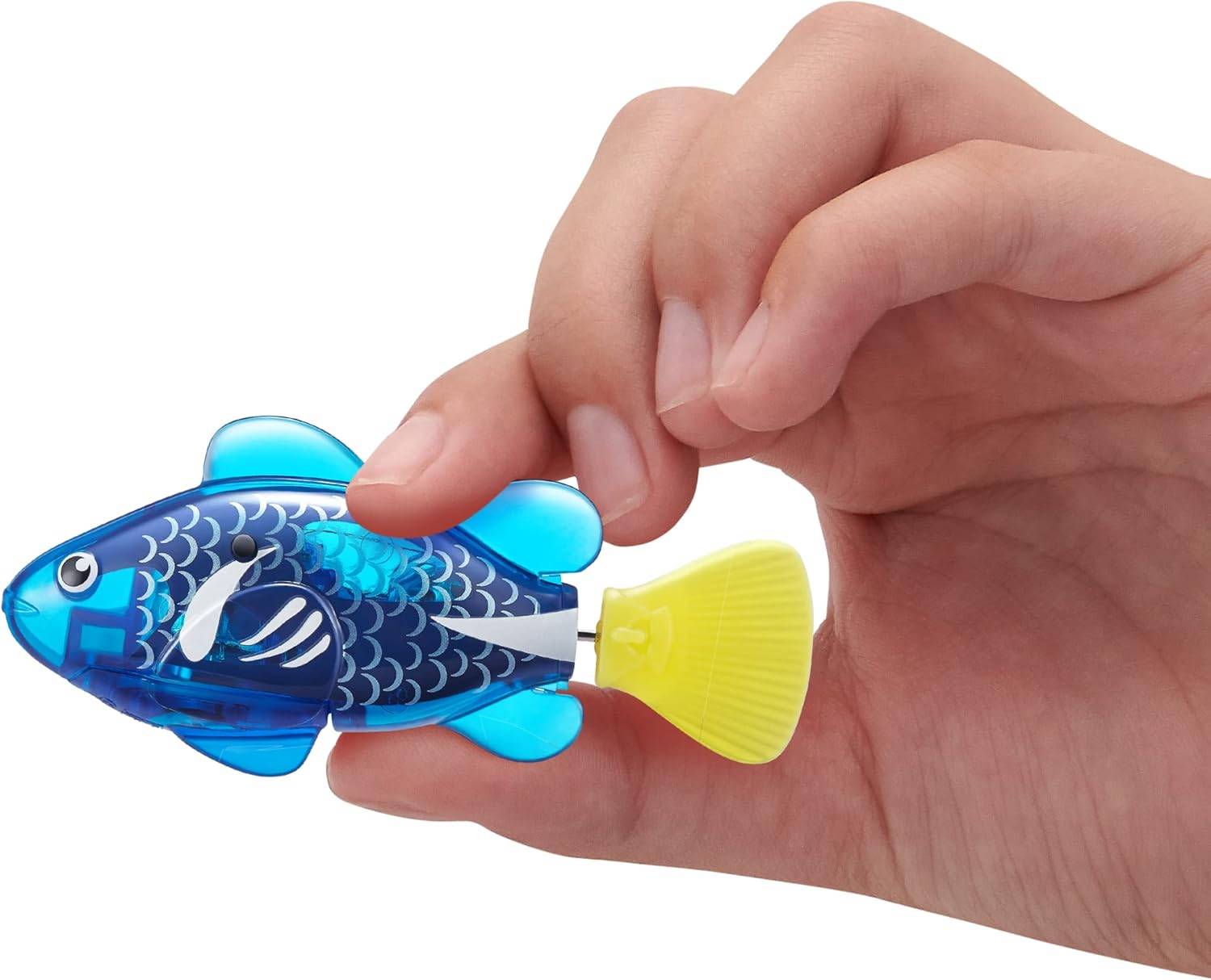 Eine Hand hält ein kleines, blaues Plastikfisch-Spielzeug mit einem gelben Schwanz. Der Fisch weist dekorative Schuppen auf und hat sichtbare mechanische Komponenten im Inneren.