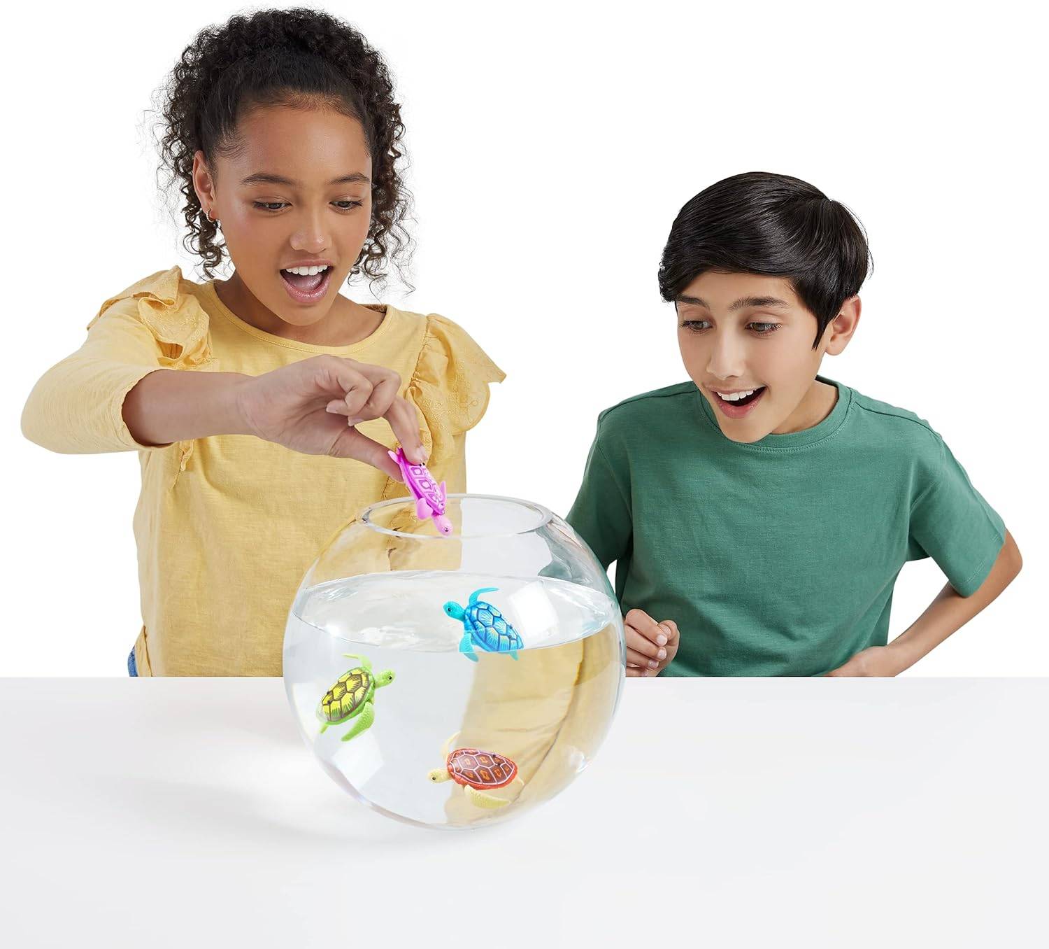 Ein Mädchen und ein Junge beobachten aufgeregt bunte Spielzeermeerestiere in einer durchsichtigen Glasschale. Das Mädchen hält einen rosa Seepferdchen, das bereit ist, hineingesetzt zu werden.