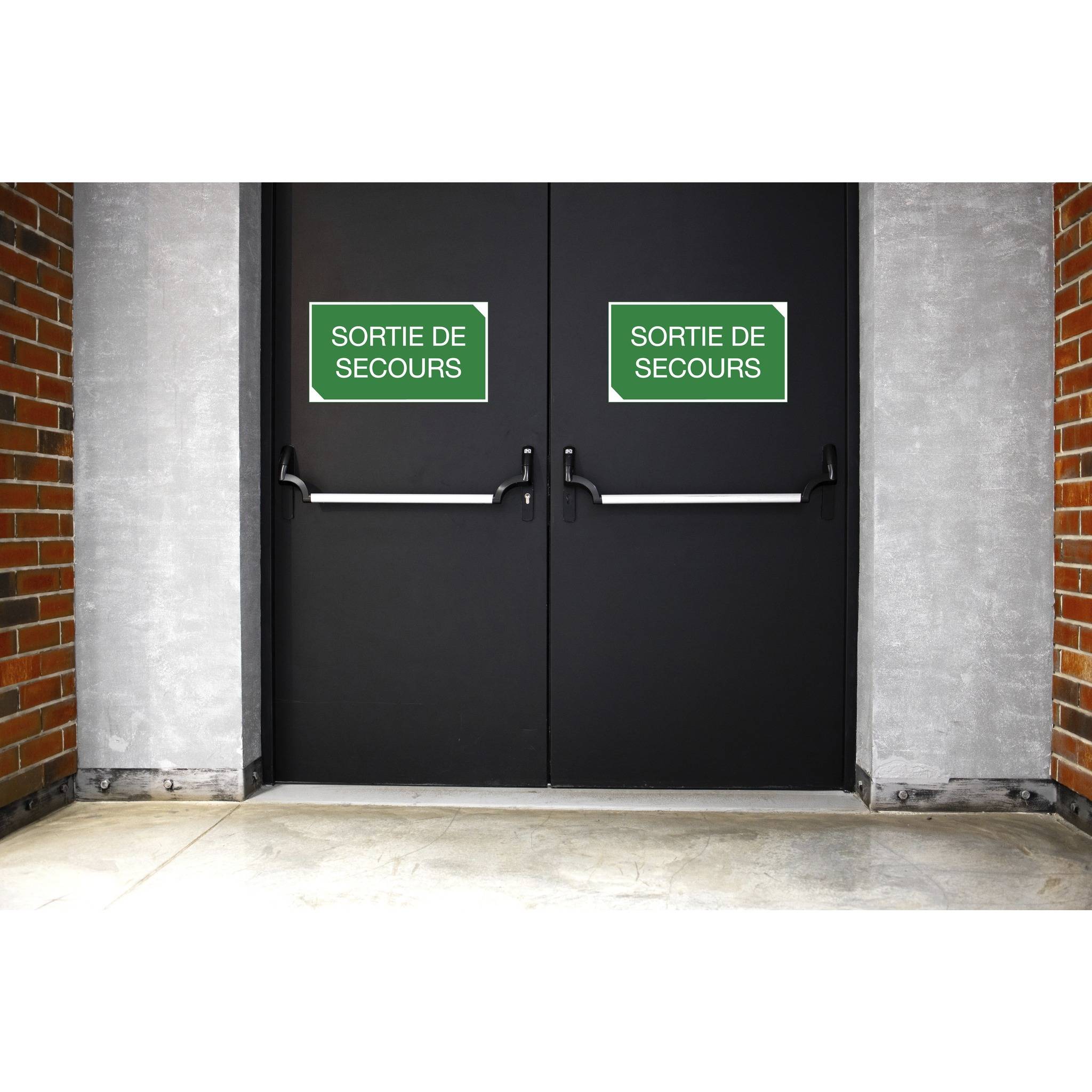 Schwarze Notausgangstüren mit zwei Schildern, die in weißer Schrift auf grünem Hintergrund ‚Sortie de Secours' tragen, positioniert zwischen Ziegelwänden.