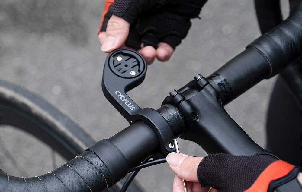 Eine Nahaufnahme einer Person, die eine Smartphone-Halterung an einem Fahrradlenker installiert, zeigt eine Hand in einem Fahrradhandschuh, die die Position der Halterung anpasst.
