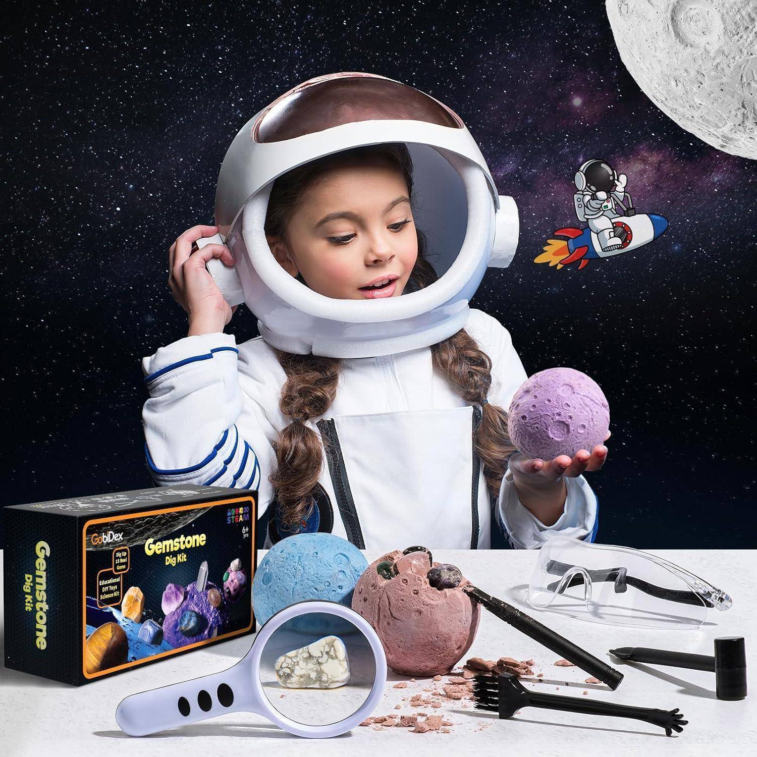 Ein Kind in einem Astronautenanzug hält einen lila Stein, umgeben von Werkzeugen und einer Kartonschachtel mit der Aufschrift „Edelstein-Ausgrabungsset