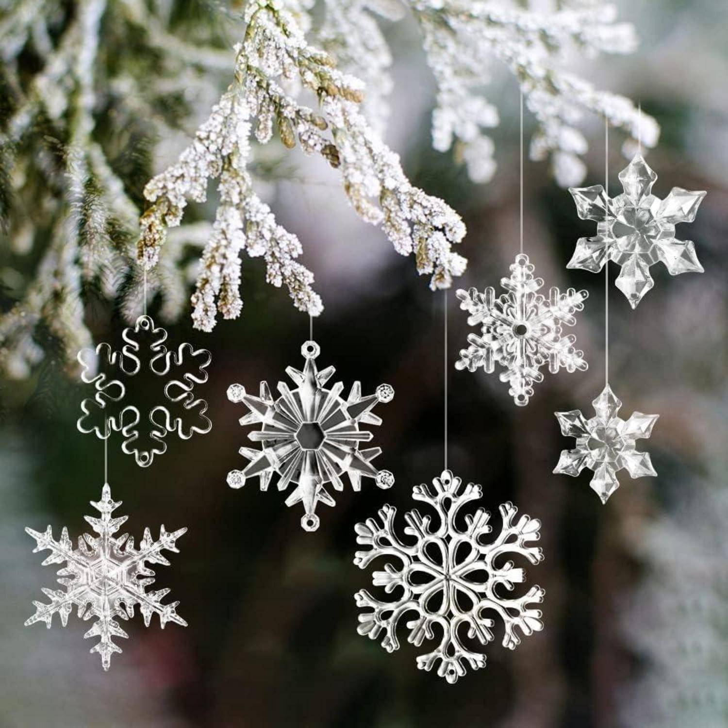 Sechs kunstvoll gearbeitete Schneeflocken-Anhänger hängen von schneebedeckten Baumzweigen und präsentieren detaillierte Designs vor einem unscharfen Naturhintergrund.