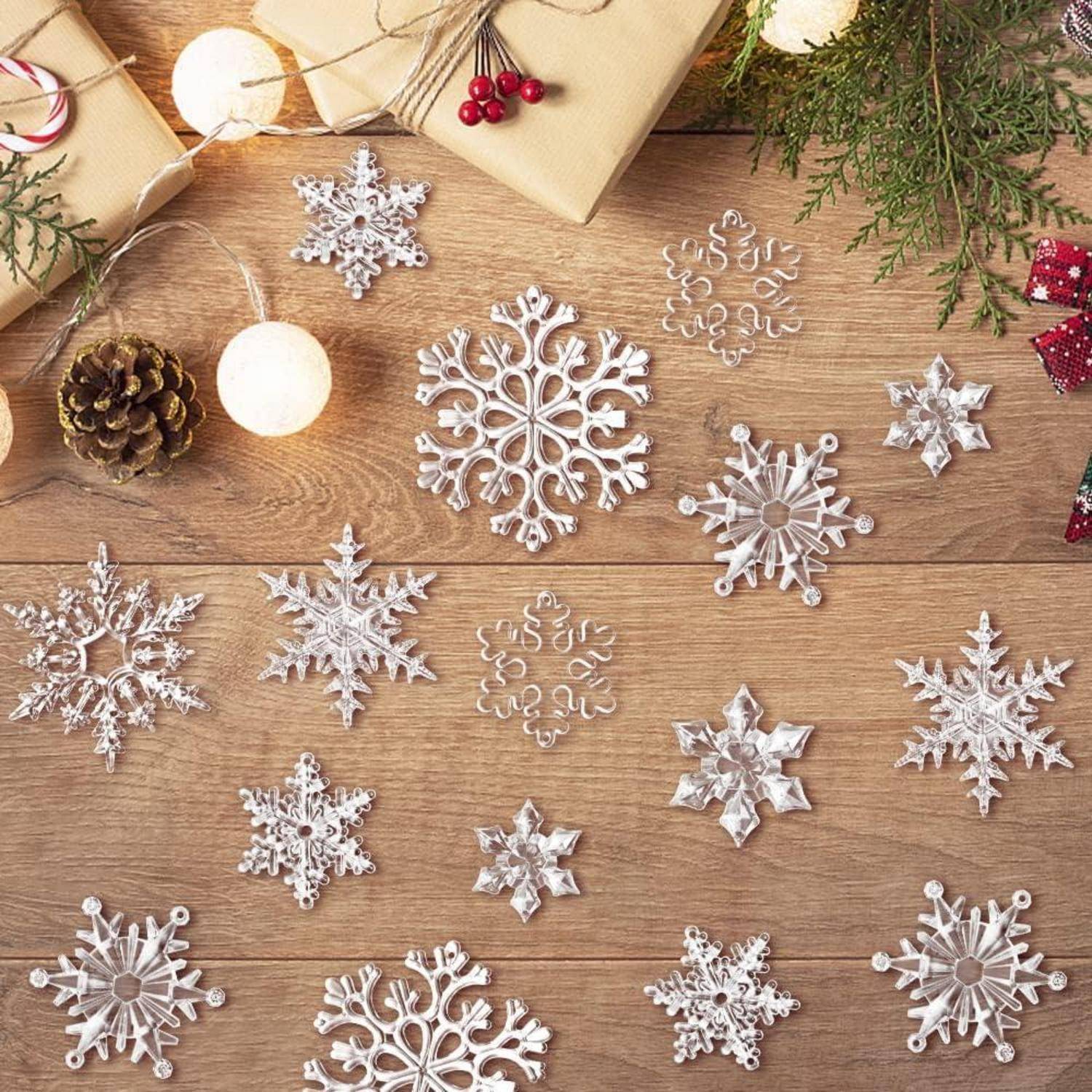 Schneeflocken-Dekorationen, die auf einer Holzoberfläche mit eingepackten Geschenken, Tannenzapfen und festlichen Lichtern angeordnet sind und eine weihnachtliche Atmosphäre schaffen.