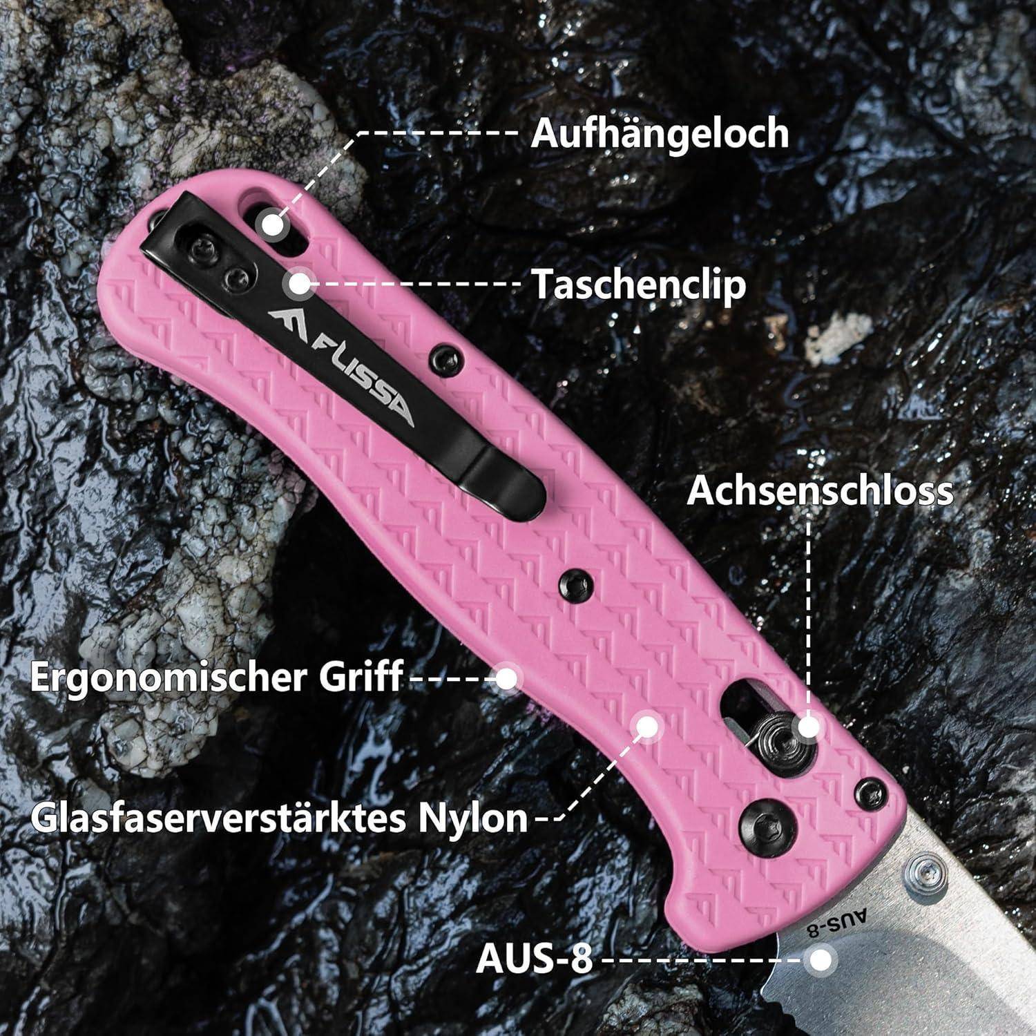 Ein pinker Messerheft mit beschrifteten Merkmalen: 'Aufhängeloch' (Aufhängeloch), 'Taschenclip' (Taschenclip), 'Achsenschloss' (Achsenschloss), 'Ergonomischer Griff' (ergonomischer Griff), 'Glasfaserverstärktes Nylon' (glasfaserverstärktes Nylon), 'AUS-8' (Stahltyp). Der Griff liegt auf einer Felsenoberfläche.
