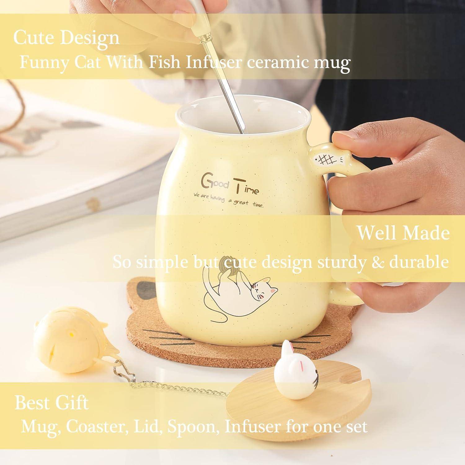 Eine Person hält eine gelbe Tasse mit einer Katzenzeichnung und dem Text 'Good Time'. Die Tasse enthält einen Fischeinsatz und wird mit einem Untersetzer, Deckel und Löffel geliefert.