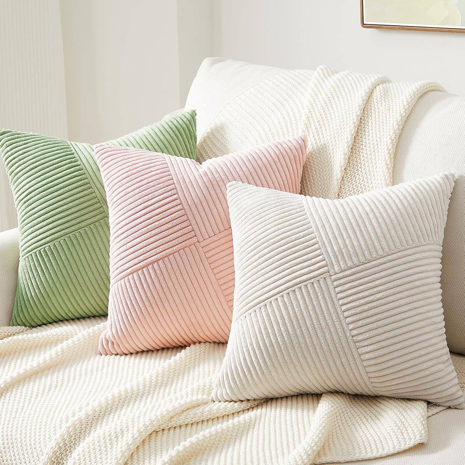 Drei dekorative Kissen mit Cordtextur in Grün, Rosa und Beige sind auf einer strukturierten, cremefarbenen Decke angeordnet.