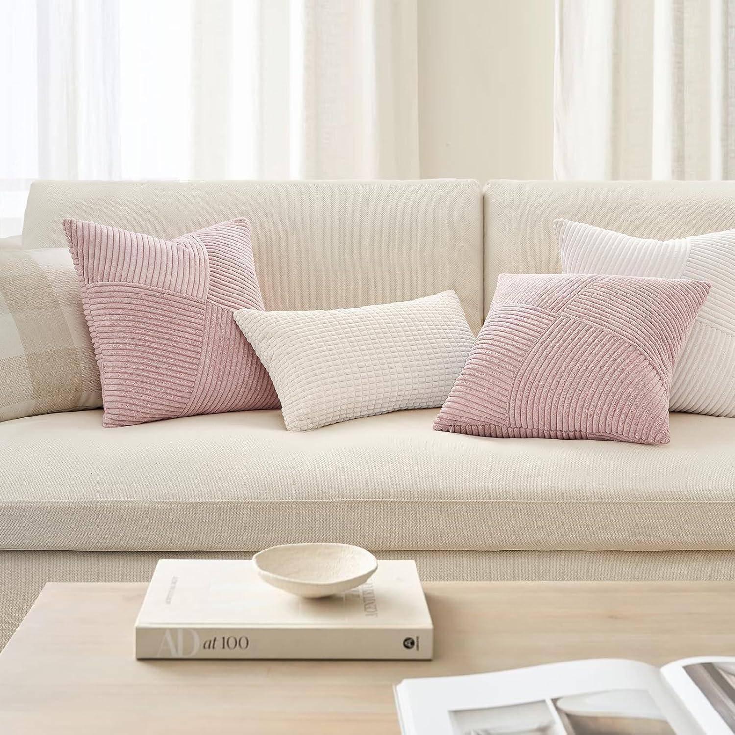 Ein beigefarbenes Sofa mit zwei rosa gestreiften Kissen und einem weißen Struktur-Kissen. Vor dem Sofa steht ein Couchtisch, auf dem ein Buch und ein runder Holztablett liegen.
