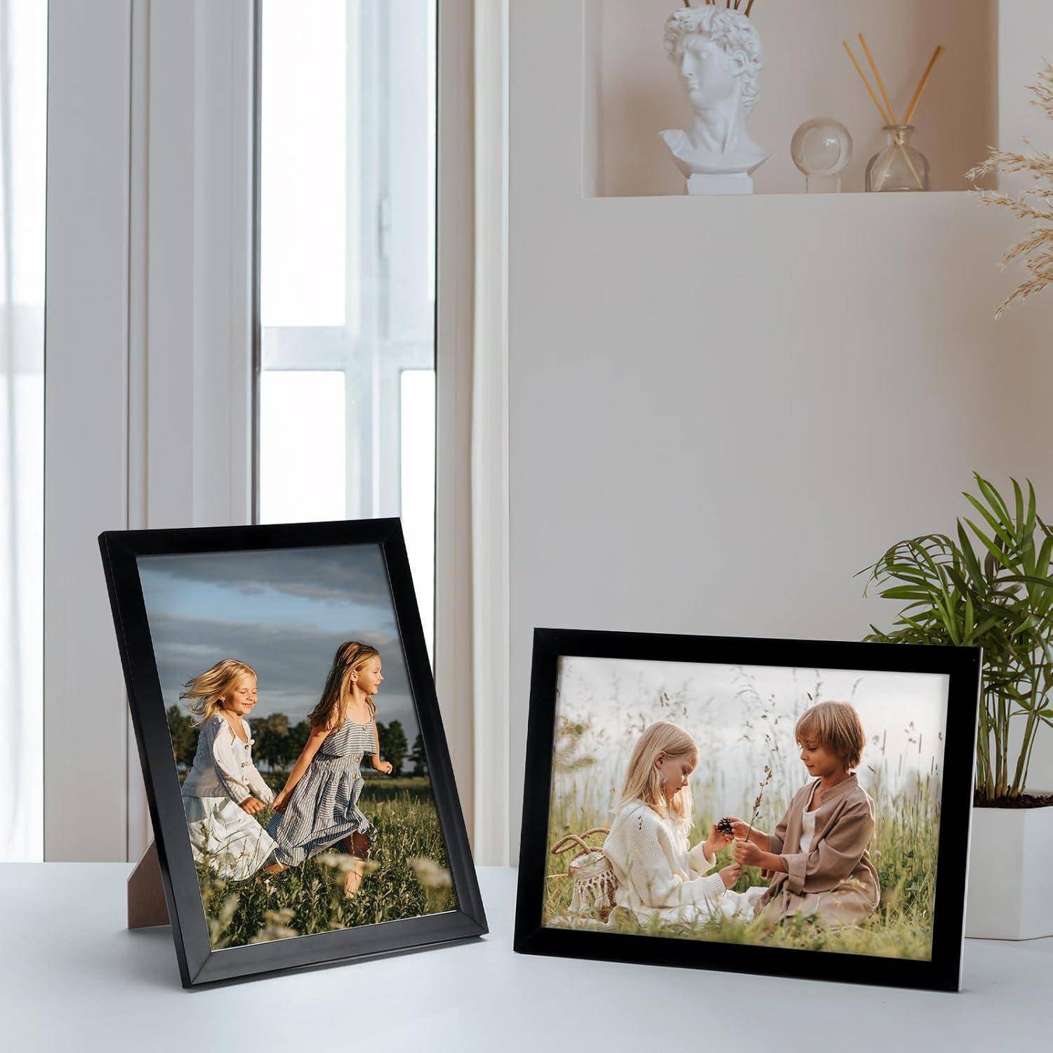 Zwei gerahmte Fotos auf einem Tisch: Eines zeigt zwei Kinder, die im Freien laufen, das andere stellt einen Jungen und ein Mädchen dar, die gemeinsam in einem Feld sitzen und eine Blume teilen.