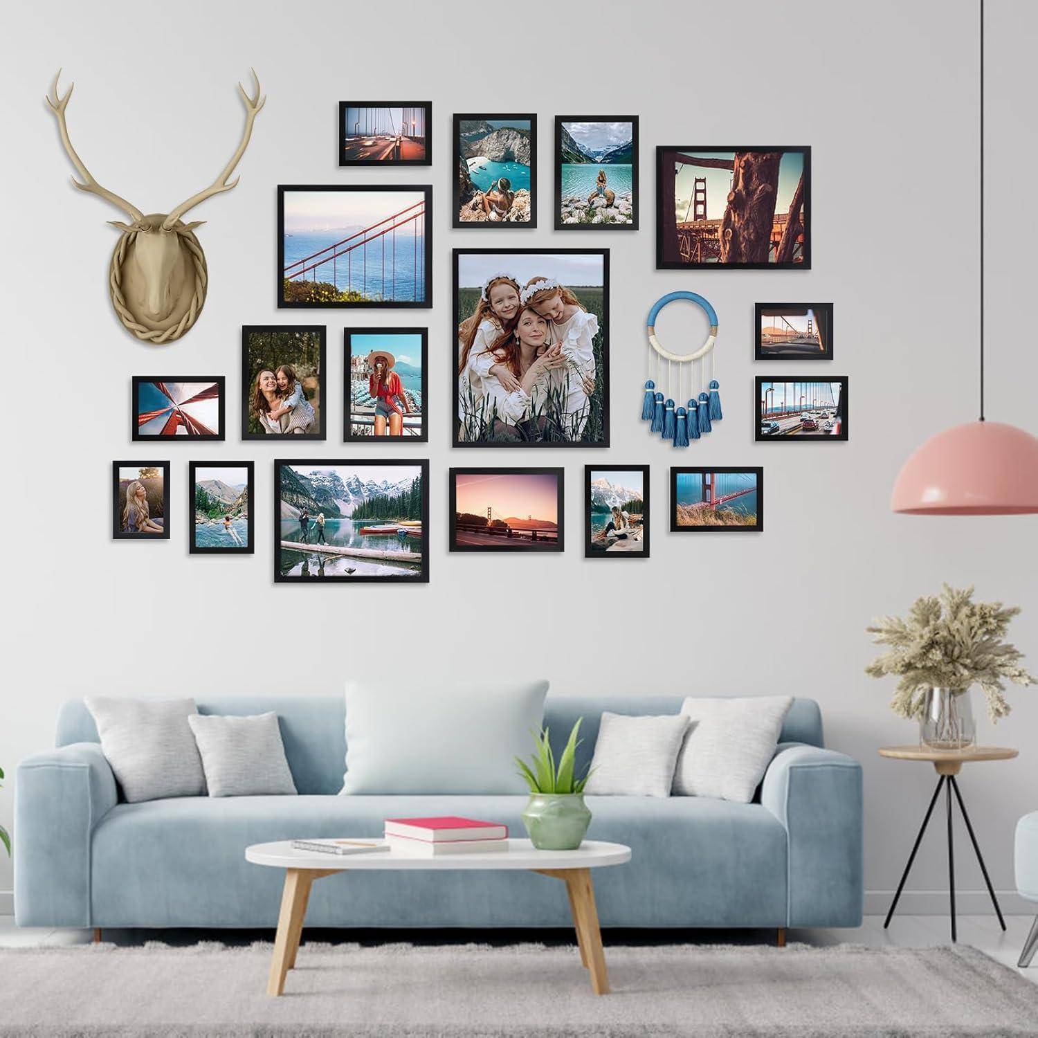 Eine Wandgalerie über einem blauen Sofa zeigt verschiedene gerahmte Fotos von Landschaften und Menschen, mit einem dekorativen Hirschkopf und Wandkunst.
