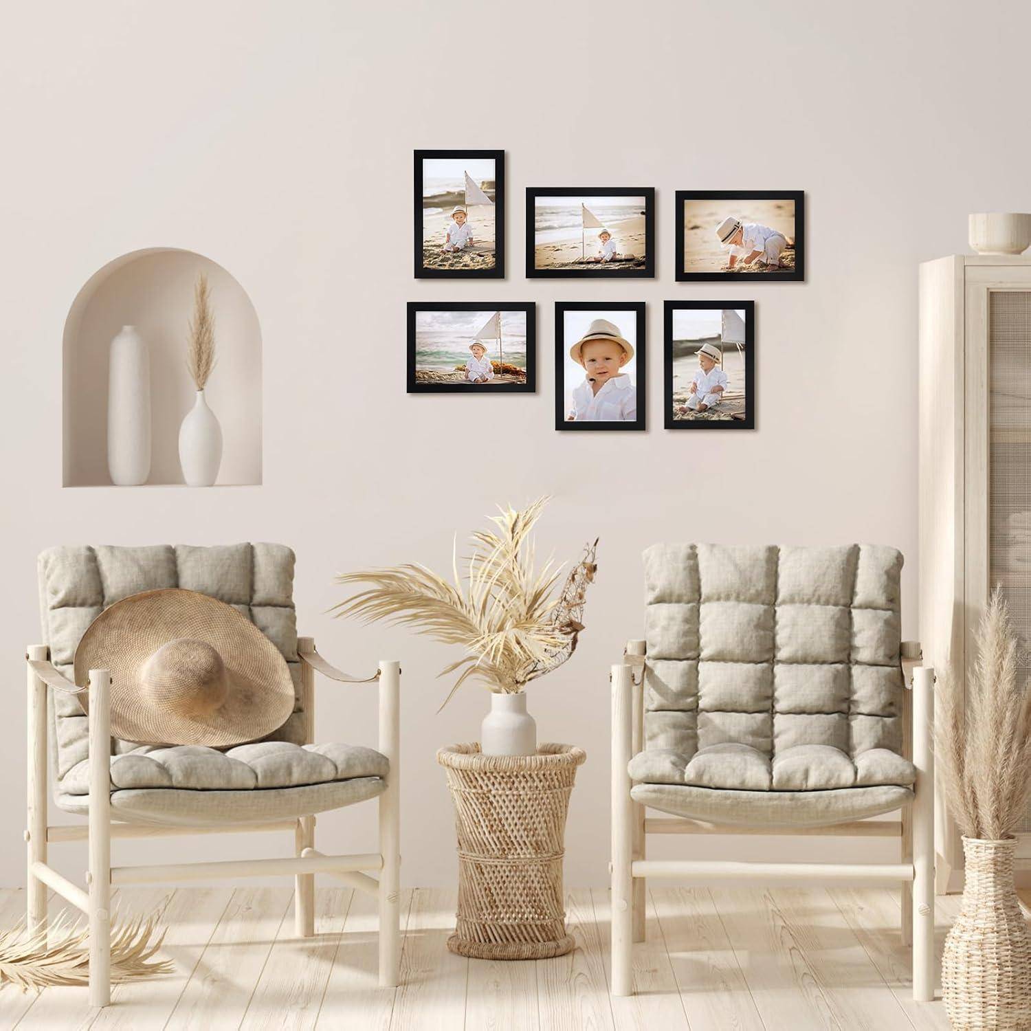 Ein gemütliches Wohnzimmer mit zwei gepolsterten Sesseln, einem Wickertisch mit getrockneten Gräsern und einer Wand mit gerahmten Fotos eines Kindes am Strand.