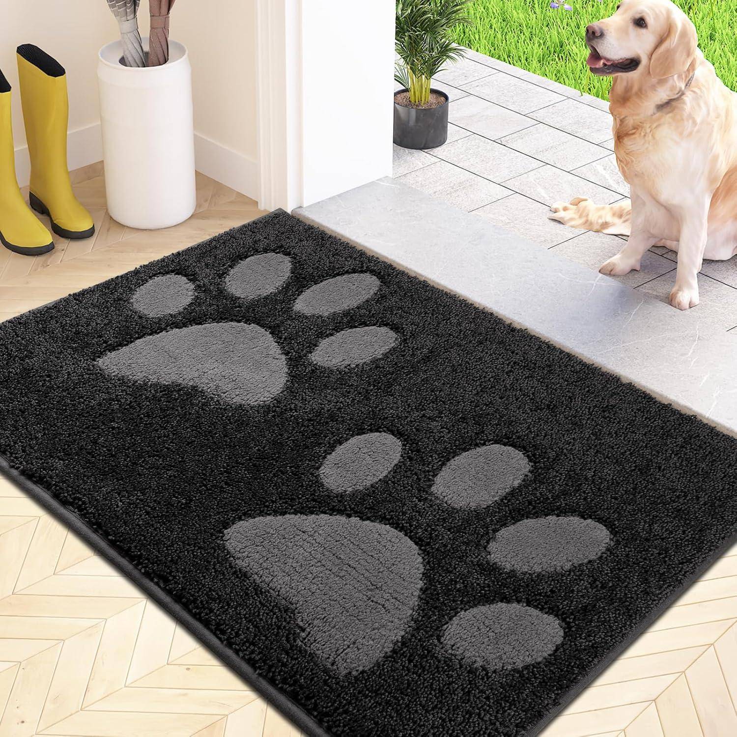 Eine schwarze Fußmatte mit großen grauen Pfotenabdrücken liegt auf einem Holzboden in der Nähe einer Tür. Ein sitzender Hund und grünes Gras sind draußen zu sehen.
