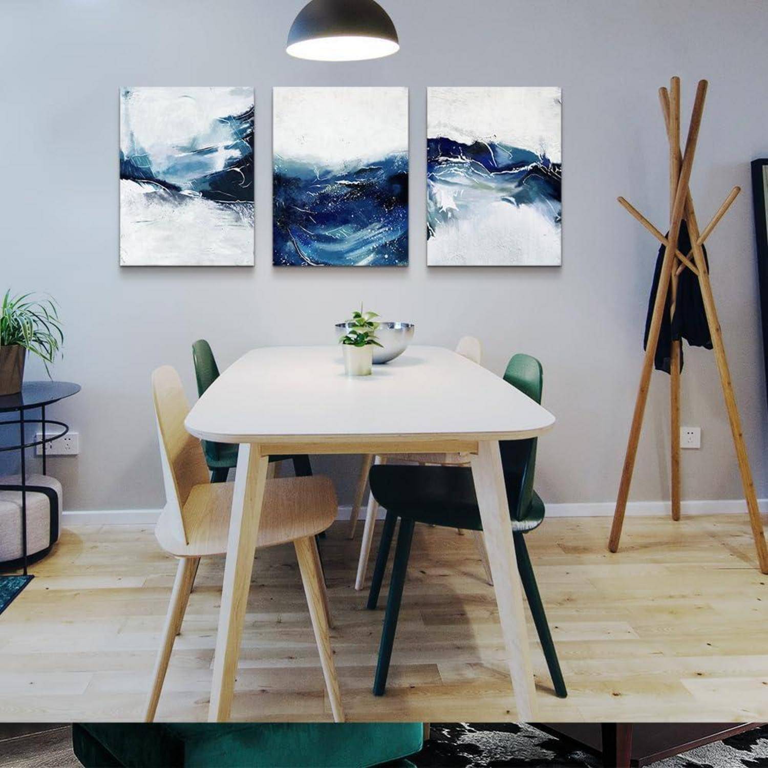 Ein Esszimmer mit einem rechteckigen Tisch, gemischten Stühlen, abstrakter blauer Kunstwerken an der Wand, einer Deckenlampe und einer Topfpflanze.