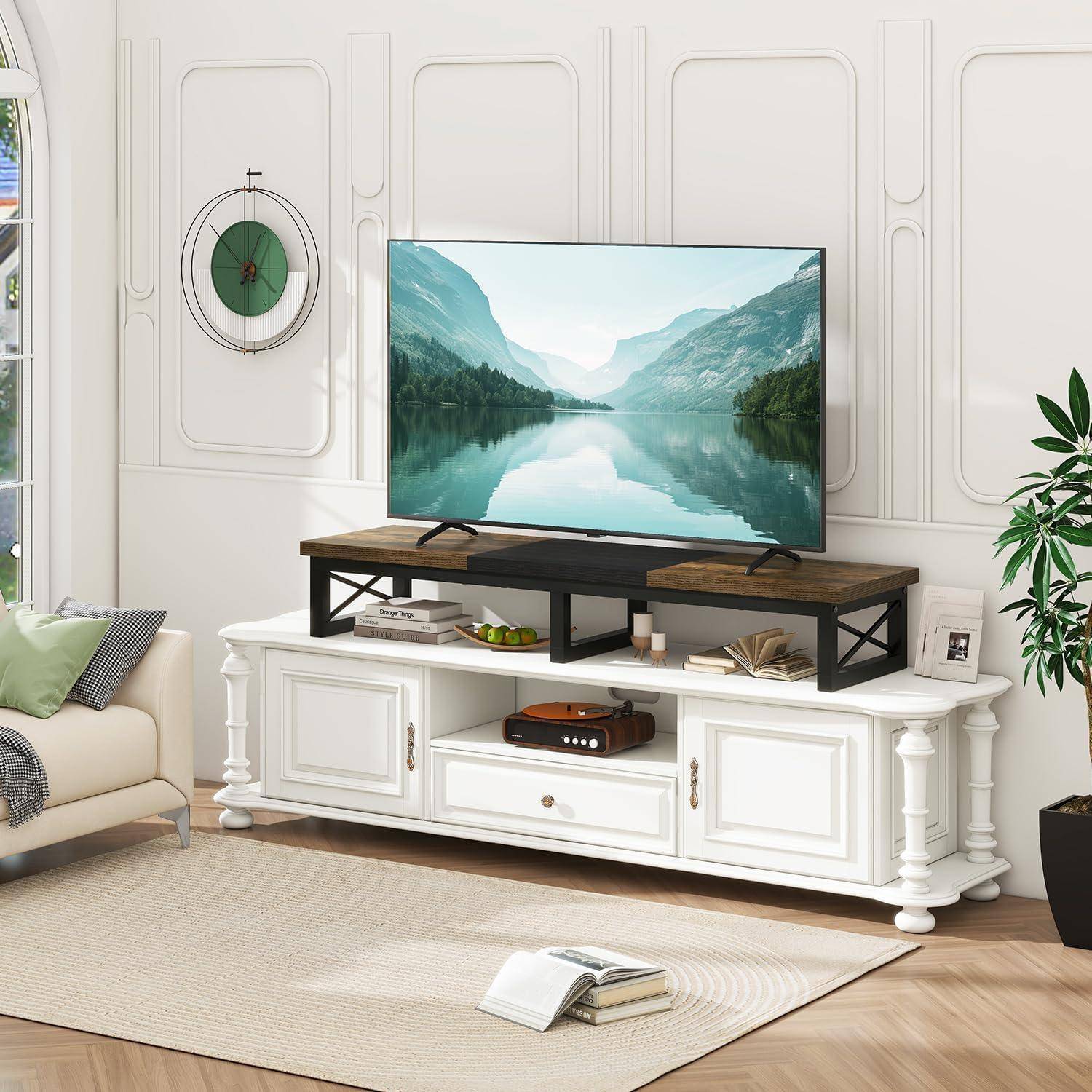 Ein Wohnzimmer mit einem weißen TV-Ständer, einem montierten Fernseher, der eine See- und Bergszene zeigt, einem beigen Sofa und dekorativen Pflanzen.