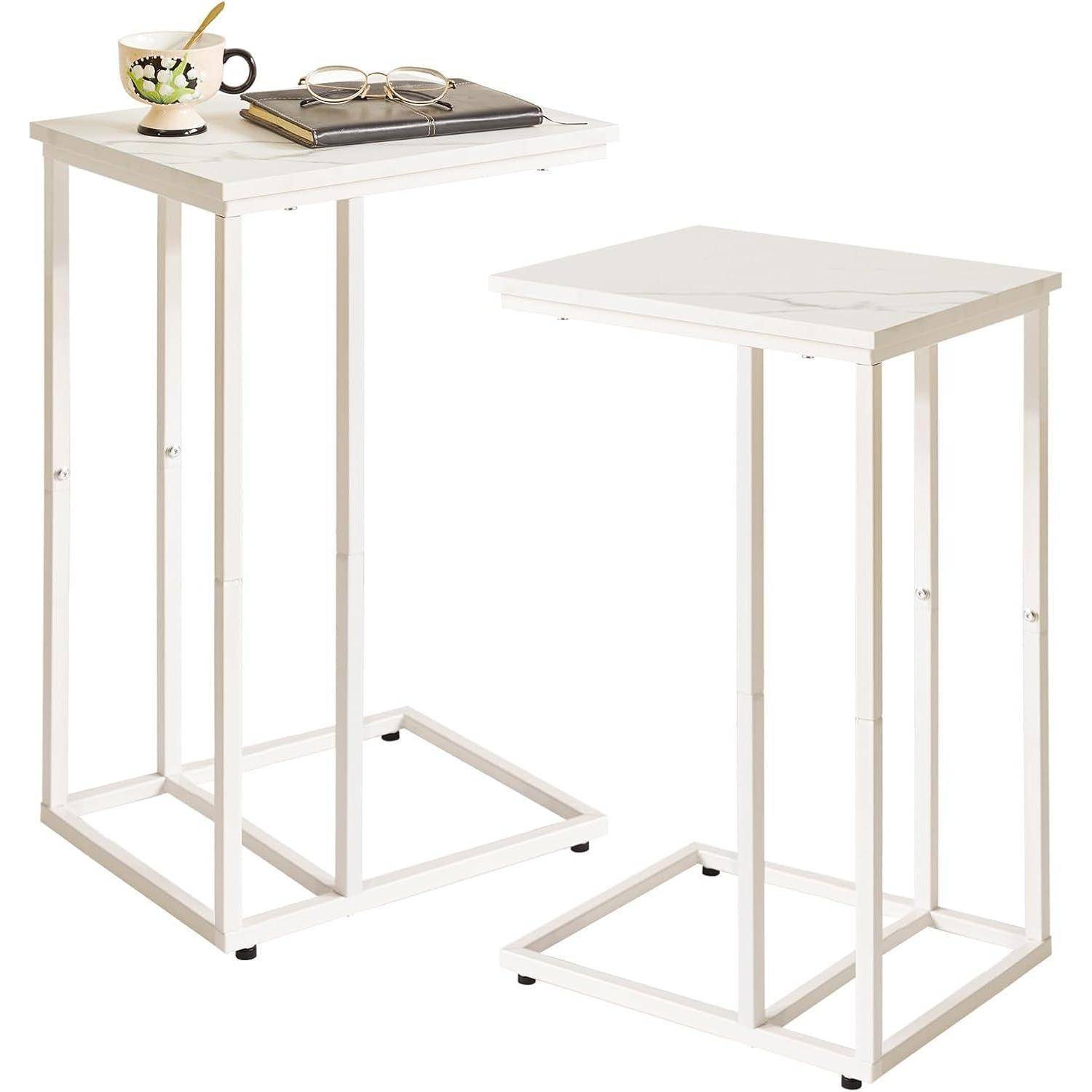 Zwei weiße, rechteckige Beistelltische mit minimalistischen Metallrahmen; einer davon trägt ein Notizbuch, eine Tasse, eine Brille und einen Bleistift, was auf einen Arbeitsbereich hindeutet.