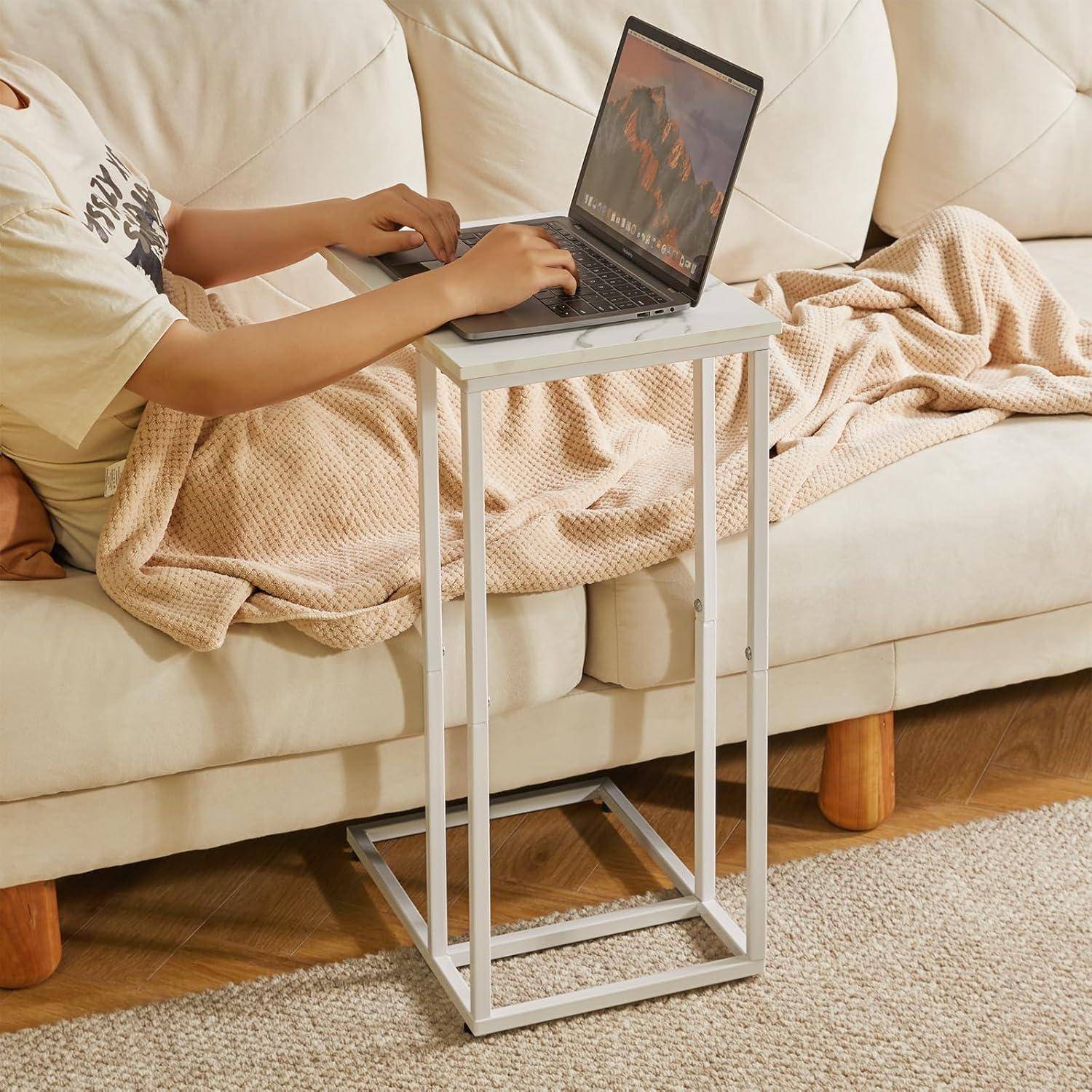 Eine Person, die auf einem Sofa sitzt und einen Laptop auf einem Ablage-Tisch benutzt, in eine beige Decke gehüllt, was einen gemütlichen häuslichen Arbeitsbereich andeutet.