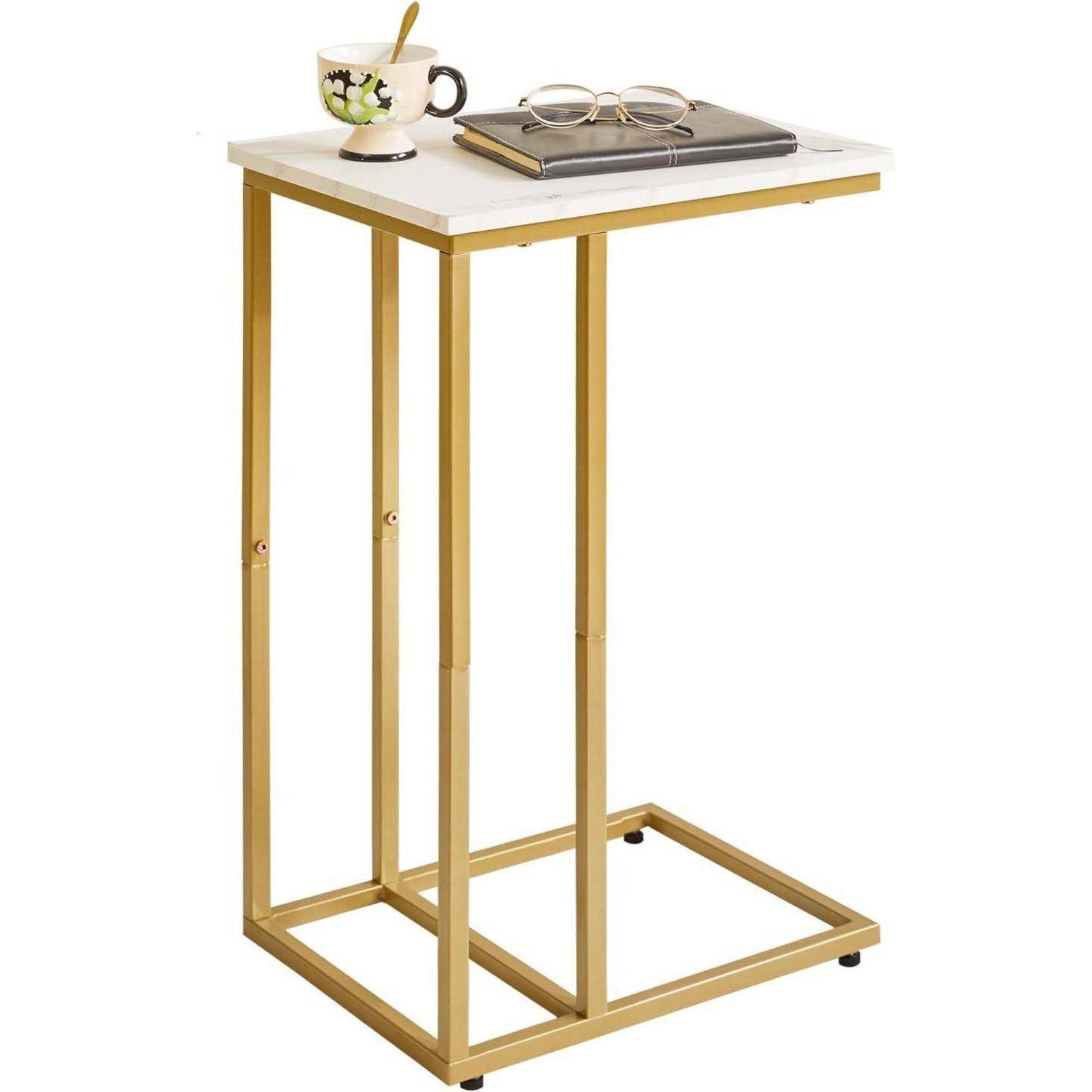 Ein kleiner Beistelltisch mit weißer Platte und goldenem Metallgestell, auf dem eine Tasse mit Blumenmuster, eine Brille und ein geschlossenes Buch stehen.