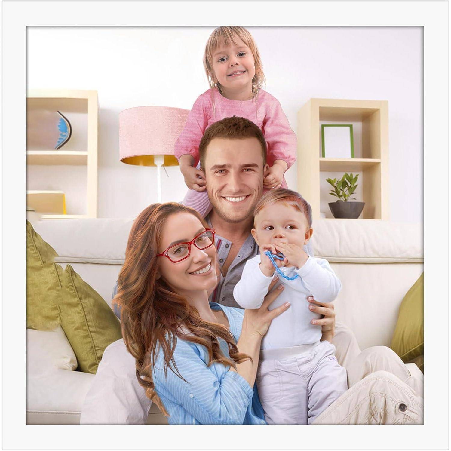 Eine lächelnde vierköpfige Familie in einem Wohnzimmer. Der Vater hält ein Baby, während die Mutter und eine kleine Tochter neben ihnen stehen. Gemütliche Atmosphäre.