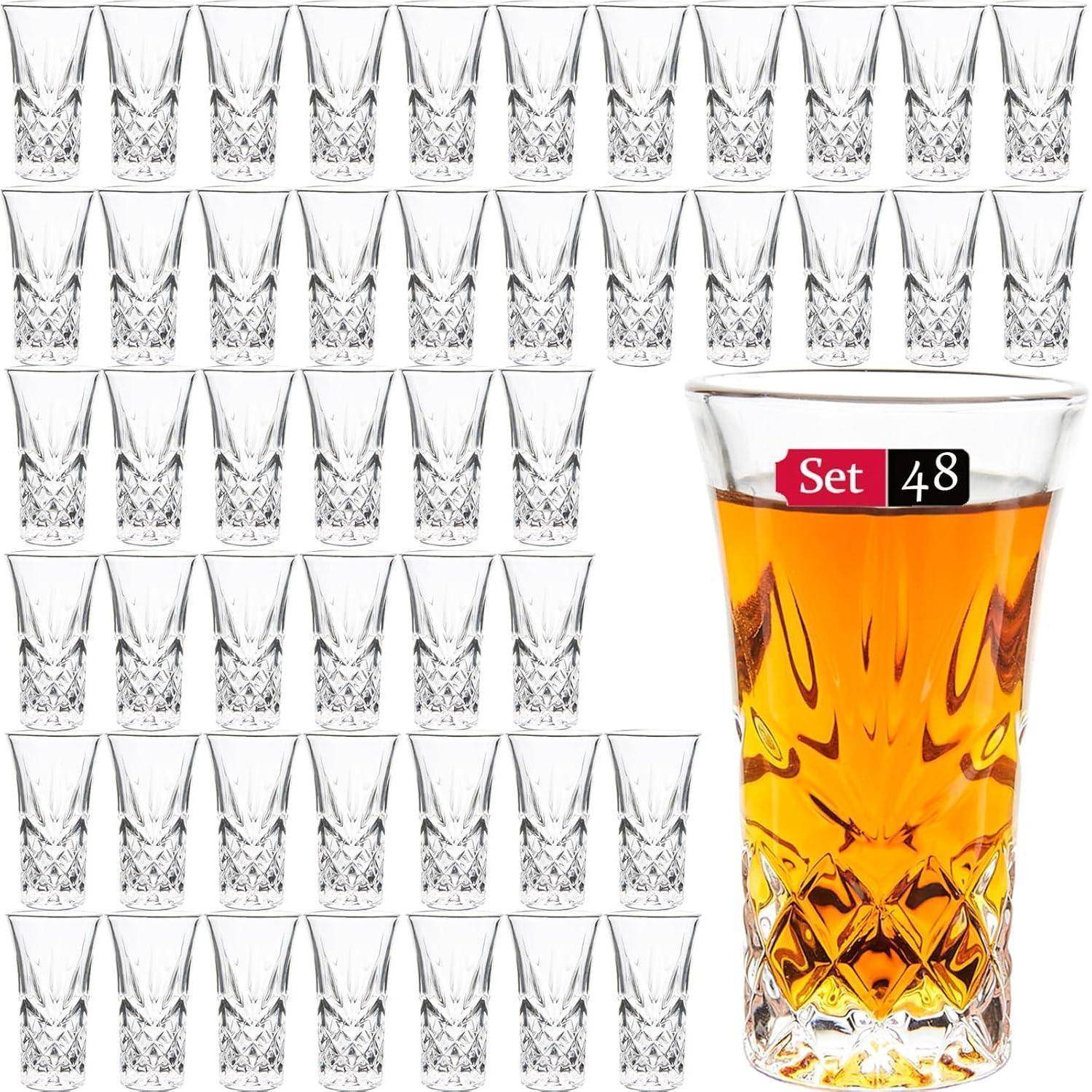 Ein großes Set von 48 klaren Kristall-Schnapsgläsern, wobei ein Glas im Vordergrund mit einer bernsteinfarbenen Flüssigkeit gefüllt ist.