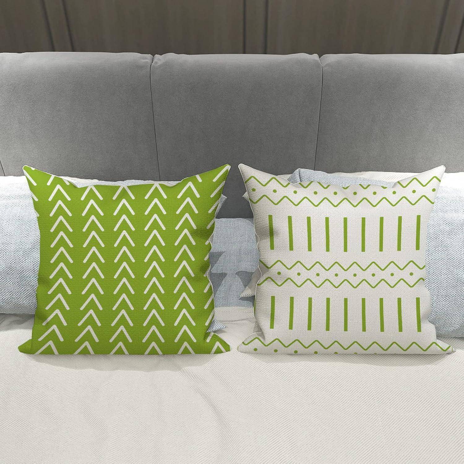Grüne und weiße Zierkissen mit geometrischen Mustern auf einem grauen Sofa. Eines hat Chevron-Streifen; das andere weist Punkte und Linien auf.