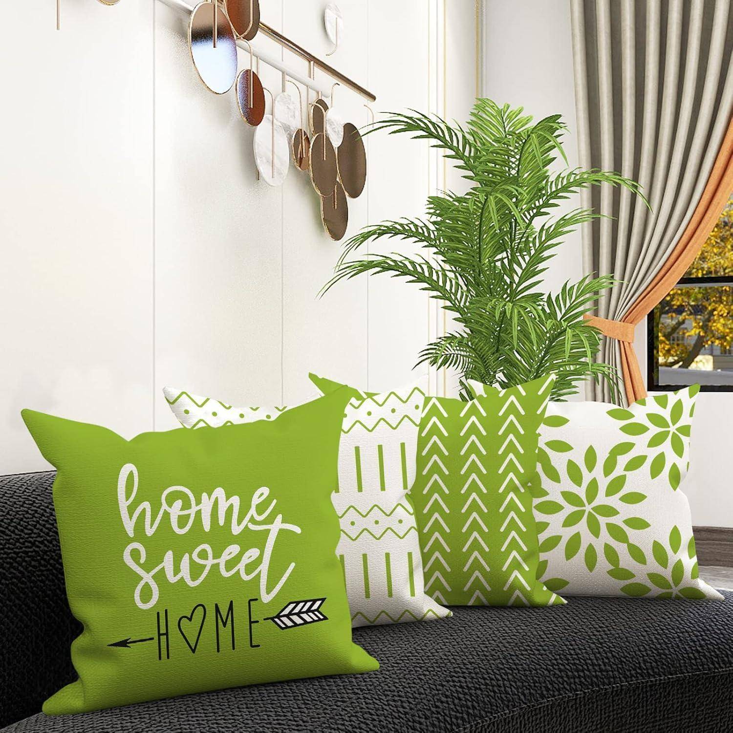 Ein Wohnzimmer-Szenario mit einem schwarzen Sofa, das grün-weiß gemusterte Kissen trägt. Ein Kissen trägt die Aufschrift ‚home sweet home'. Eine kleine Pflanze steht neben dem Sofa.