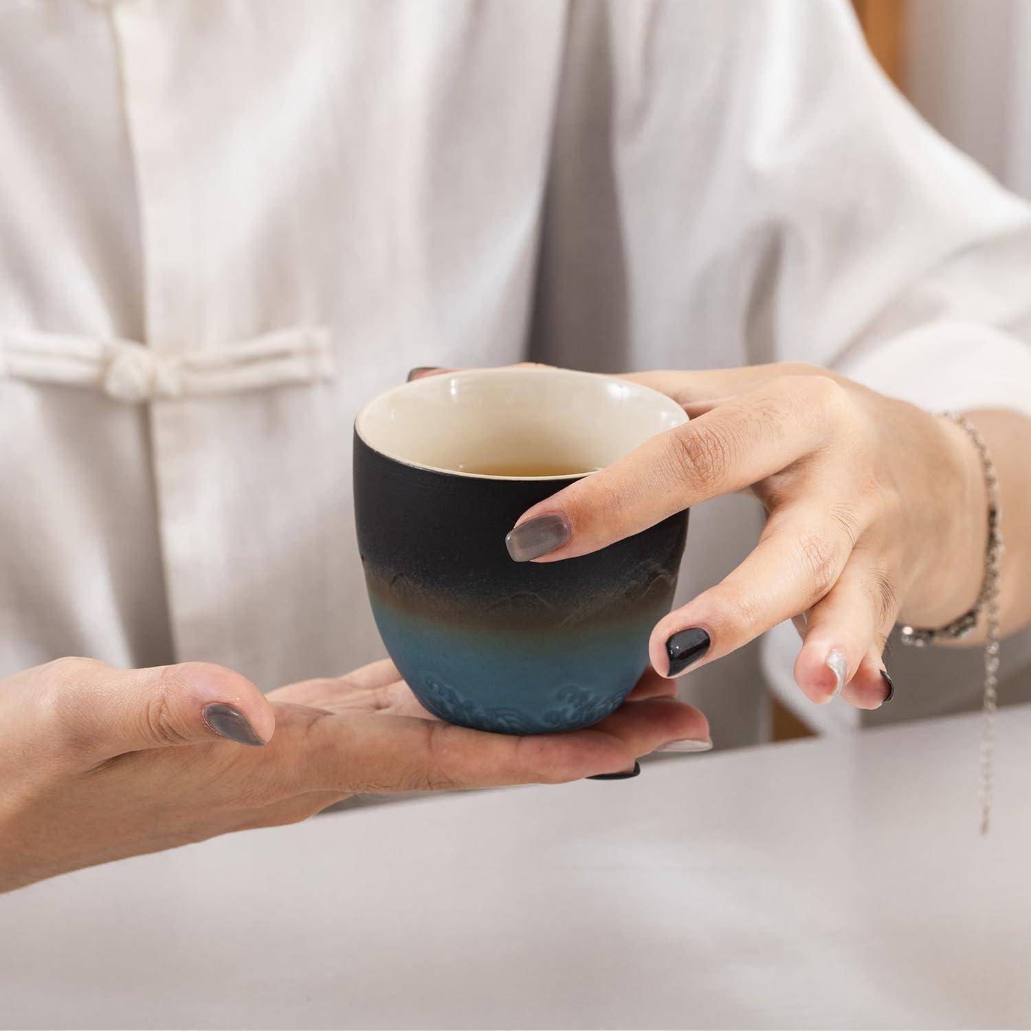 Eine Person in einem weißen Gewand hält eine blaue Keramiktasse mit einem heißen Getränk in der Handfläche und vermittelt damit einen entspannten Moment.