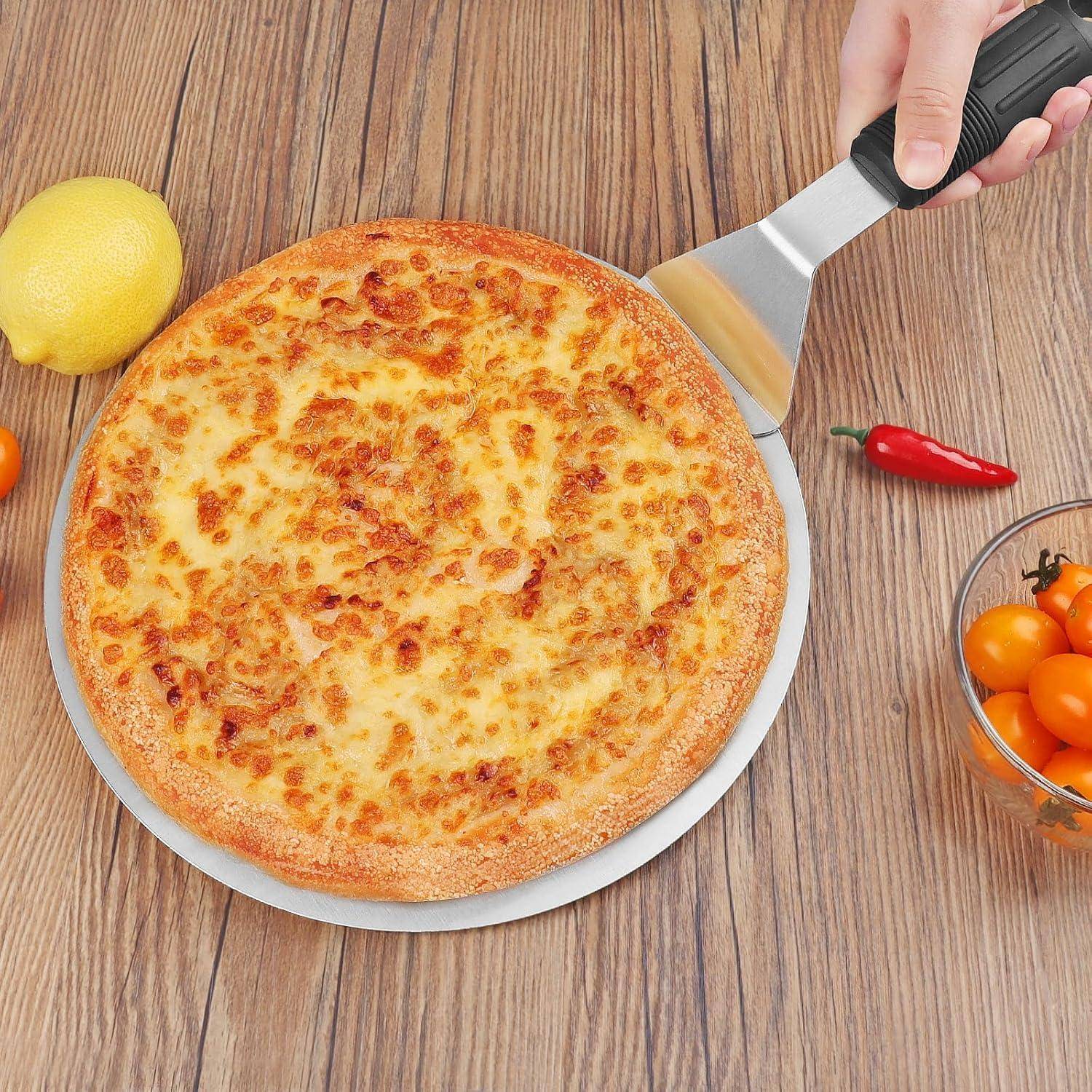 Eine Hand verwendet einen Pizzaschneider, um eine käsige Pizzascheibe auf einem Holztisch anzuheben, wobei eine Zitrone, eine rote Chilischote und eine Schüssel mit Kirschtomaten in der Nähe liegen.