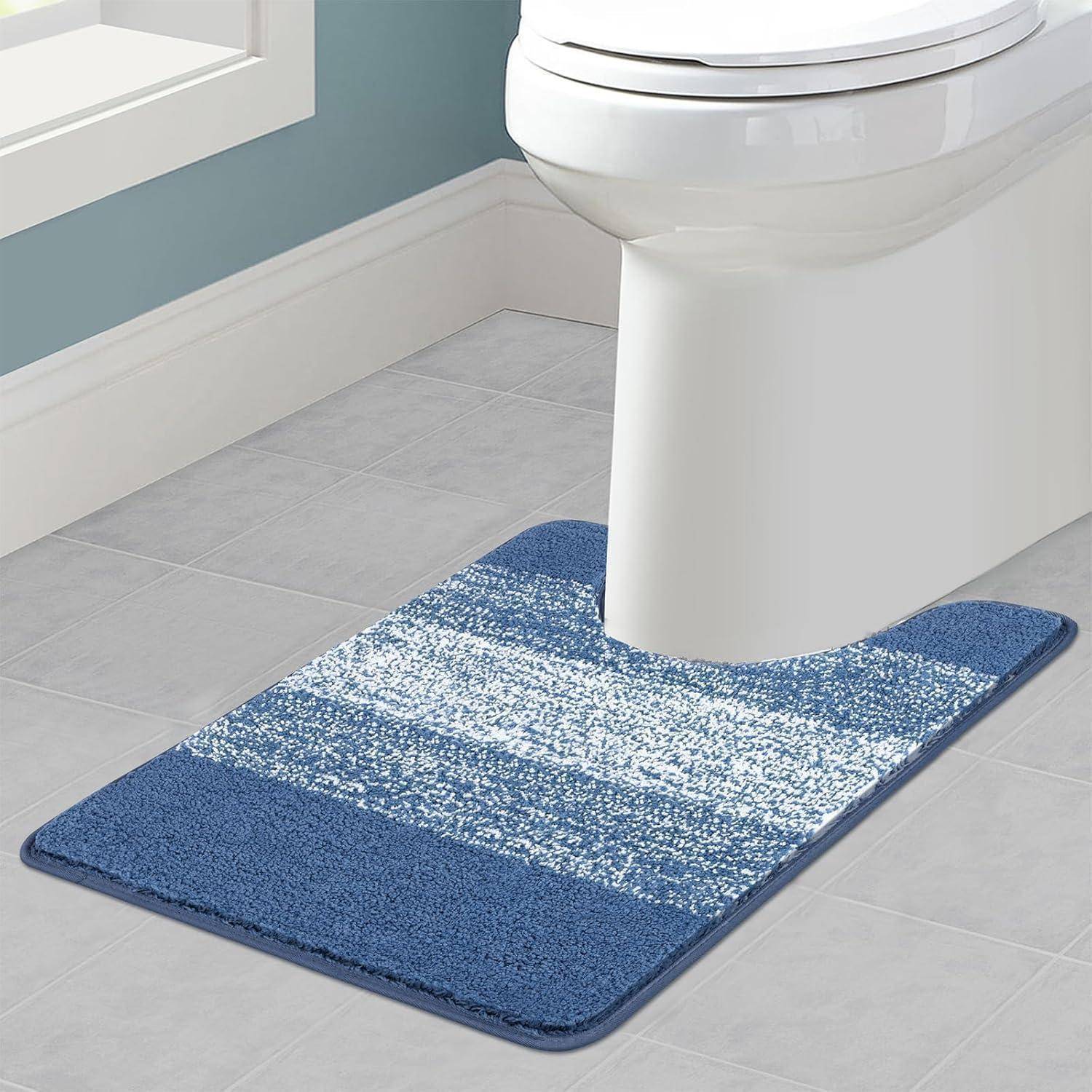 Ein blau verlaufendes Badezimmerteppich liegt auf einem hellgrauen gefliesten Boden, vor einer weißen Toilette an einer blassen blauen Wand.